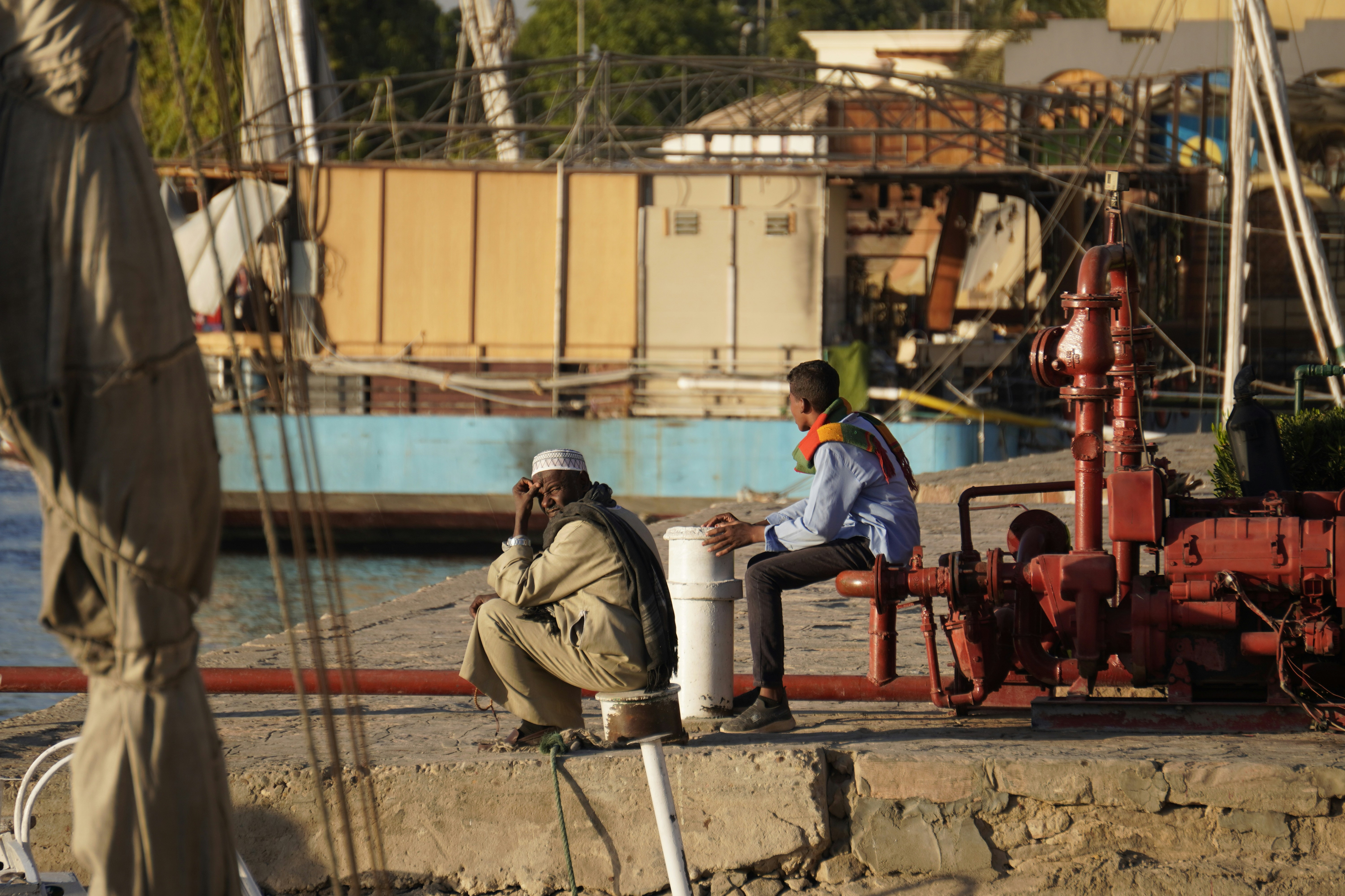 Construction workers wearing safety helmets and harnesses, perhaps taking a water break in the shade, emphasizing the importance of safety and breaks.