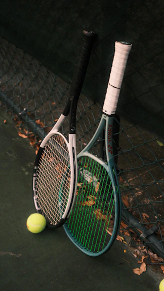 Two tennis rackets leaning against a chain link fence