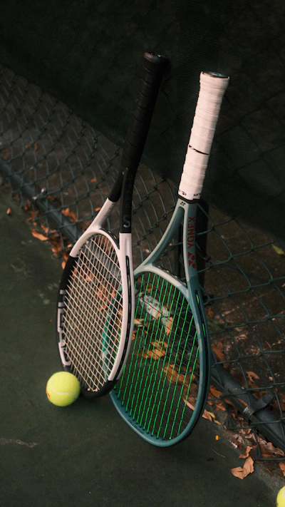 Two tennis rackets leaning against a chain link fence