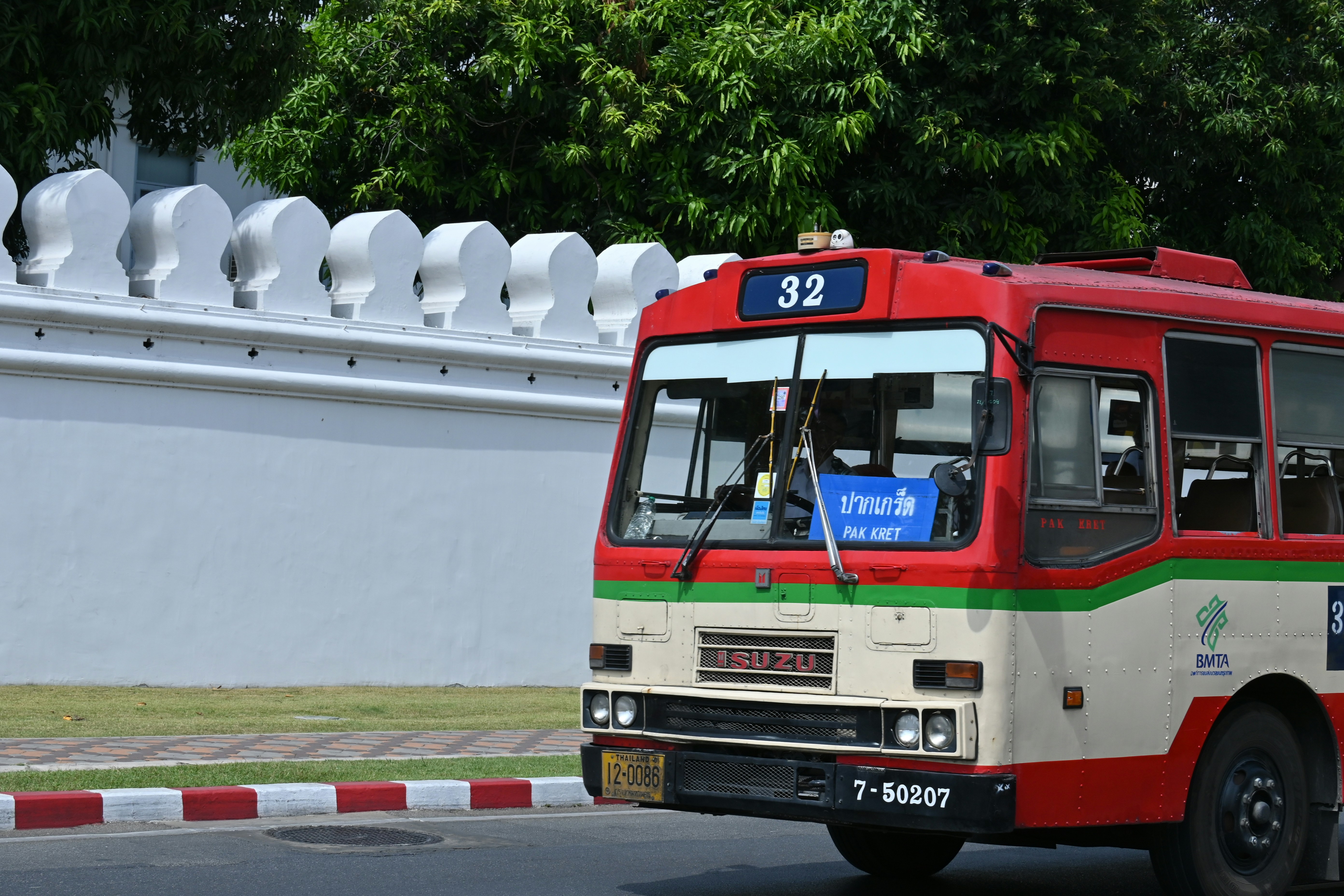 A red bus driving down a street next to a white fence