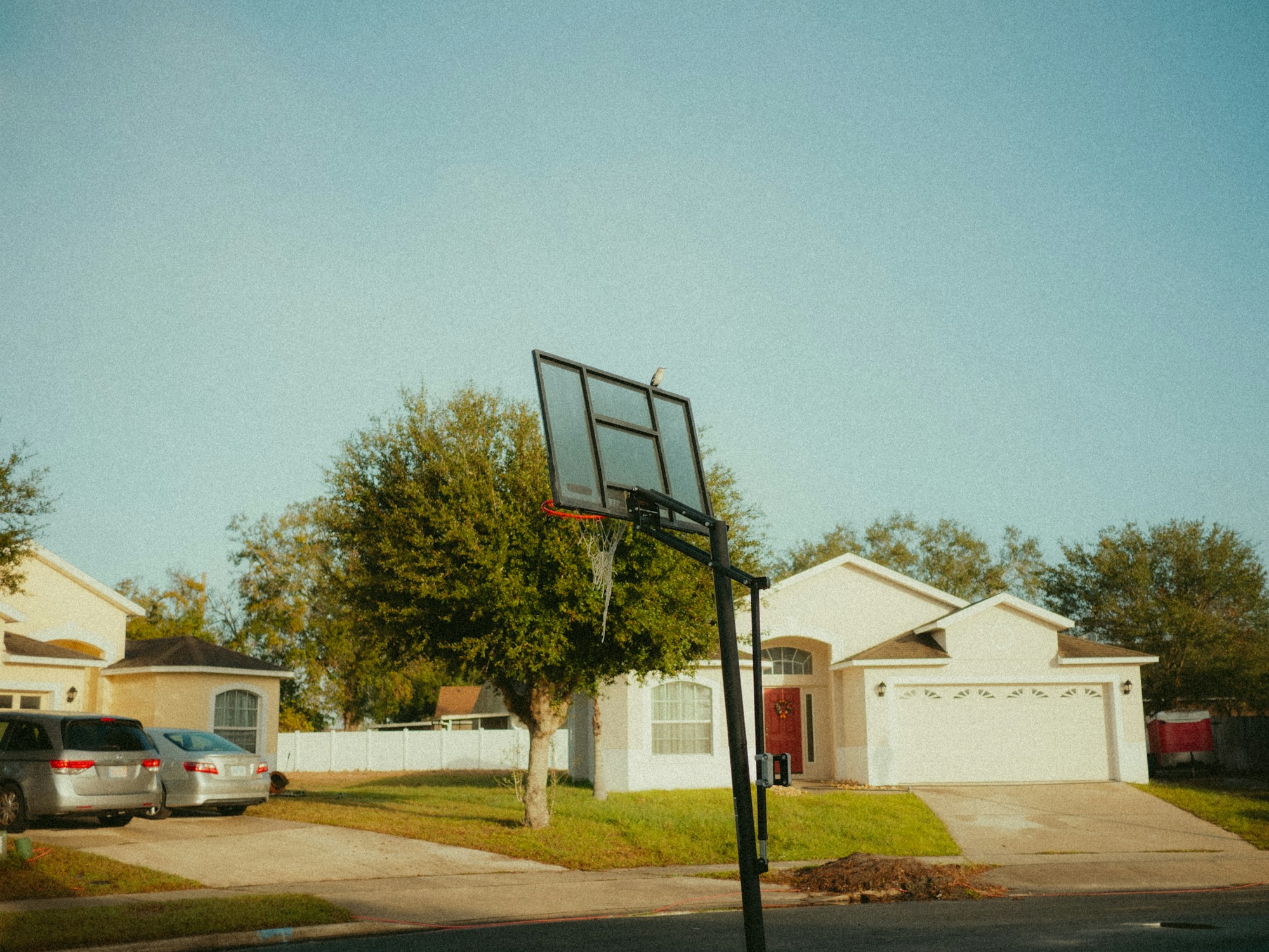 A basketball hoop standing in a driveway in front of a suburban house