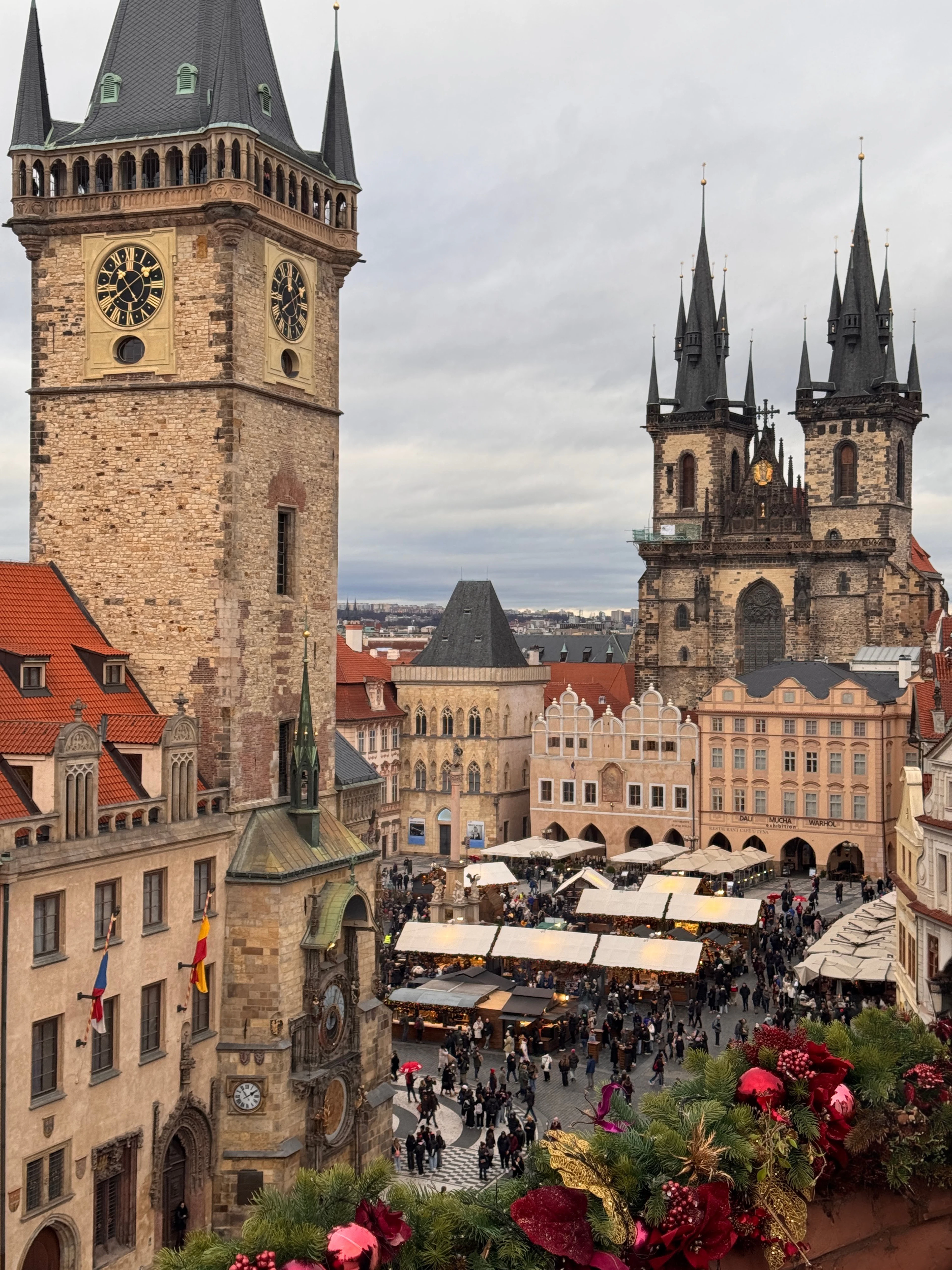 Old Town Square's Christmas market glows beneath the illuminated Astronomical Clock tower and Tyn Church at dusk.