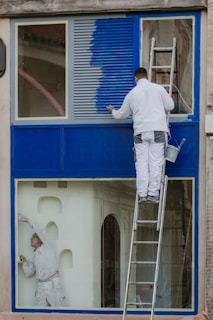 A man painting a window with a ladder