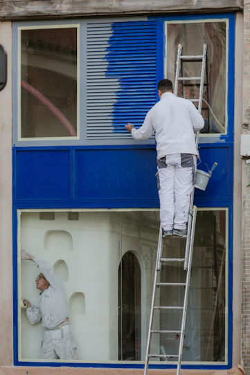 A man painting a window with a ladder