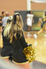 Two cheerleaders in black and gold outfits on a basketball court