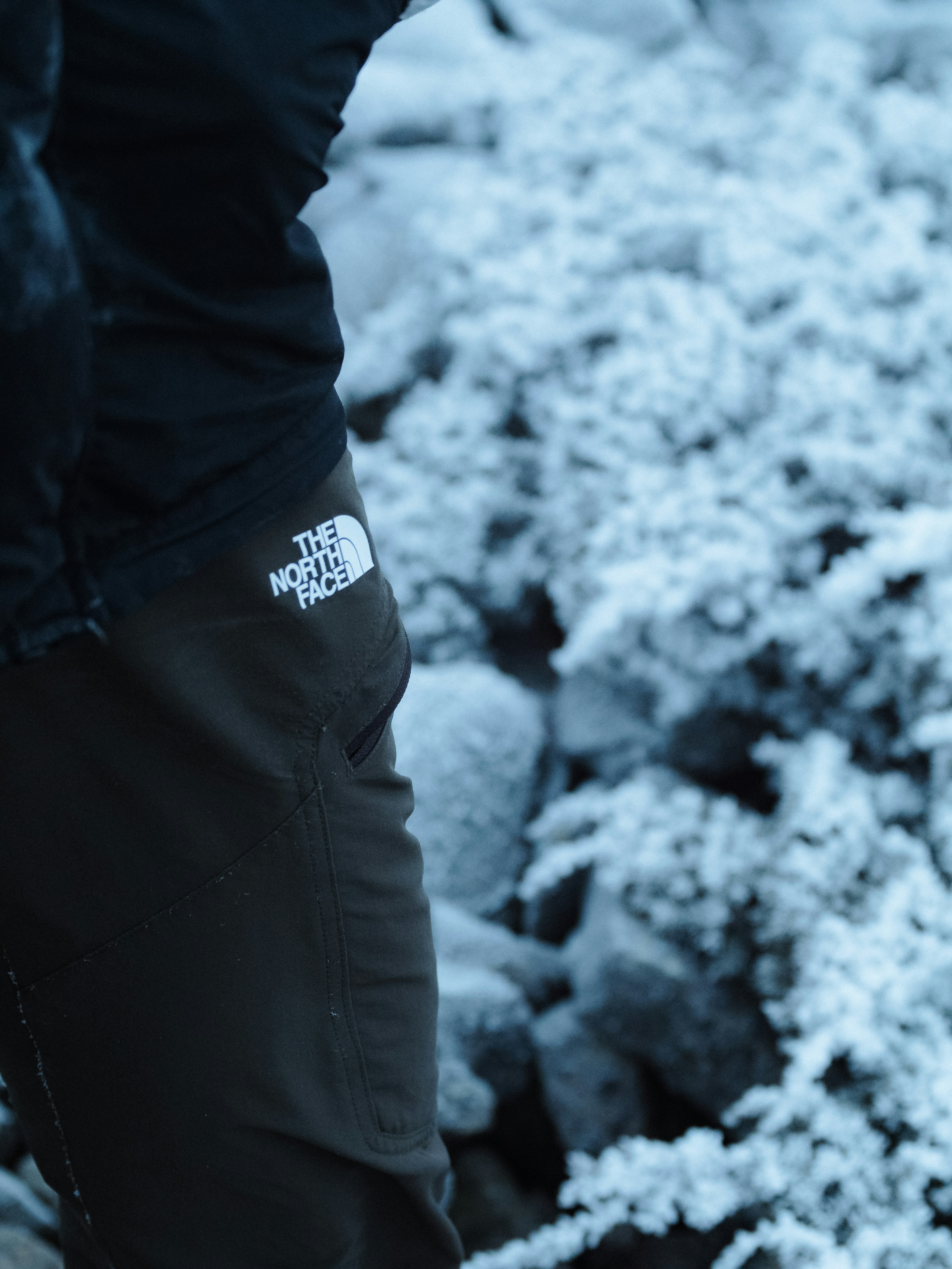 A person standing on a rocky beach covered in snow