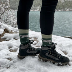 A person standing on snow covered ground next to a body of water