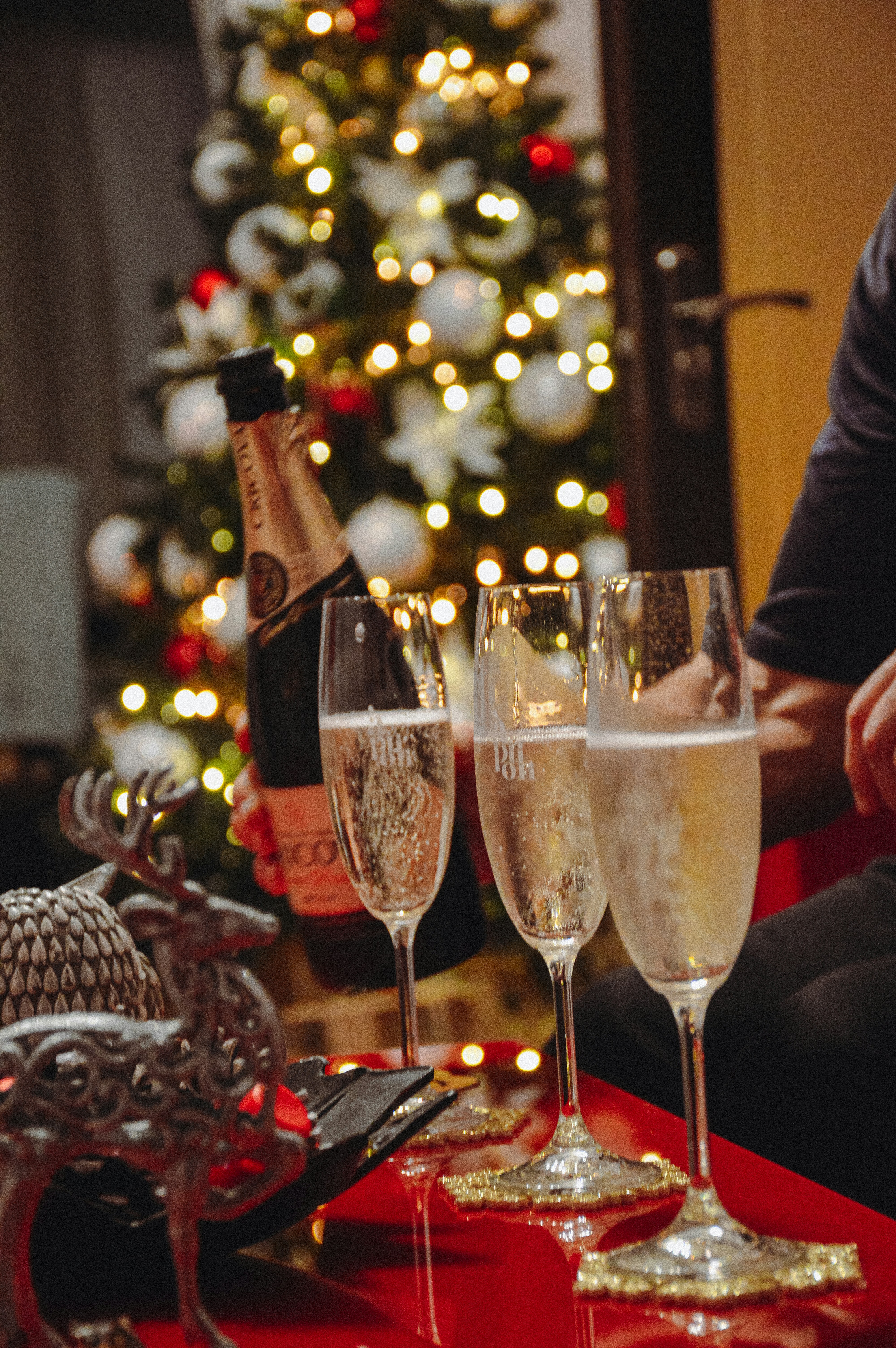 A man sitting in front of a christmas tree with three glasses of champagne
