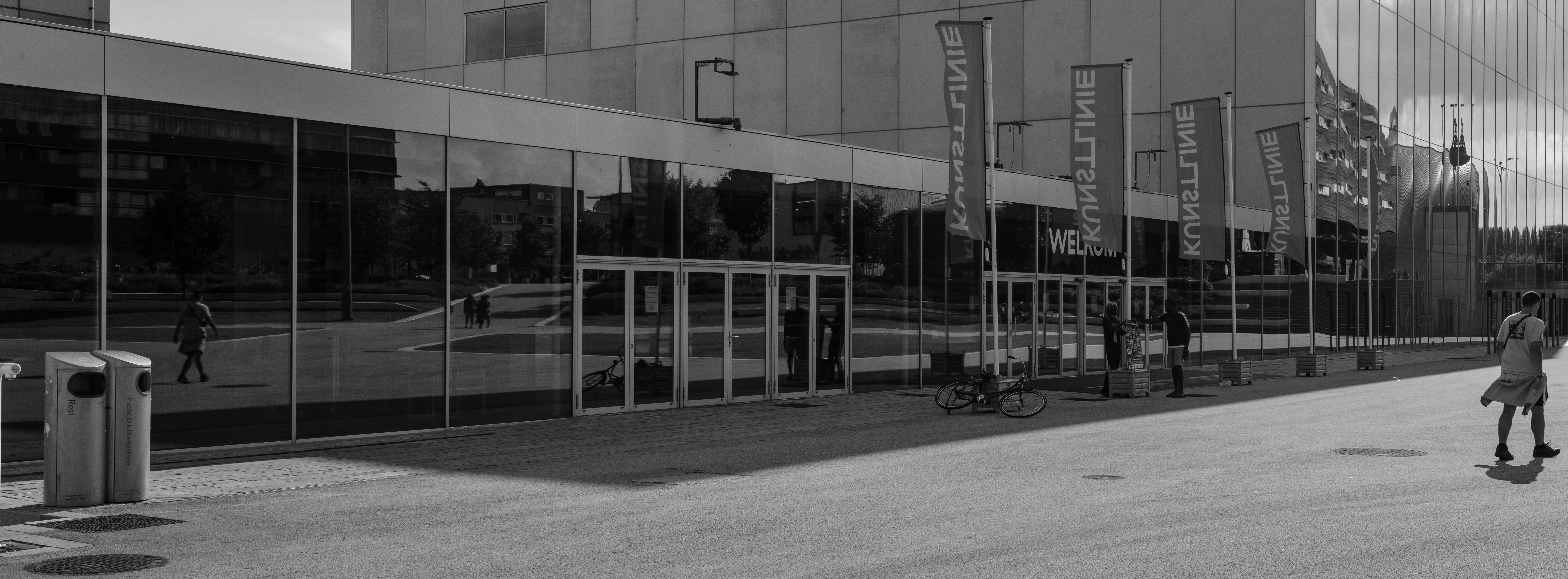 A black and white photo of a person walking in front of a building