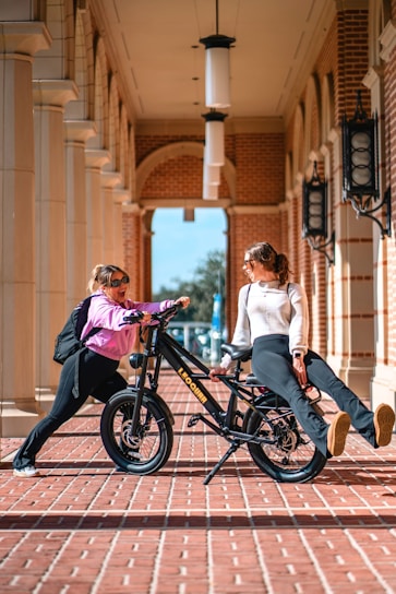 A woman sitting on top of a bike next to another woman