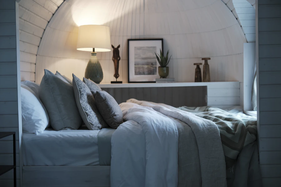 Windowless cabin with a made bed, layered linens and a warm bedside lamp