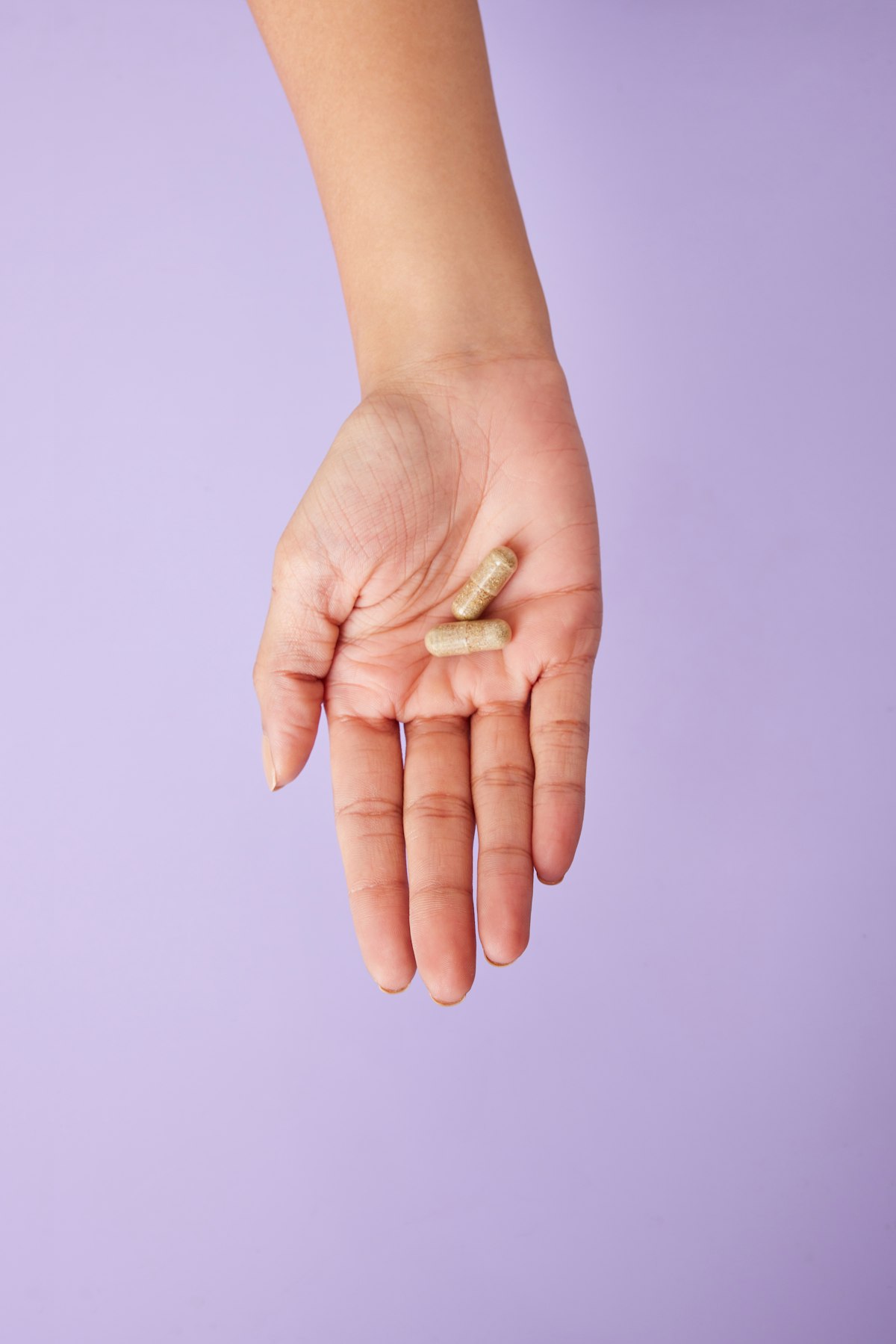 A hand holding a single capsule beside a glass of water