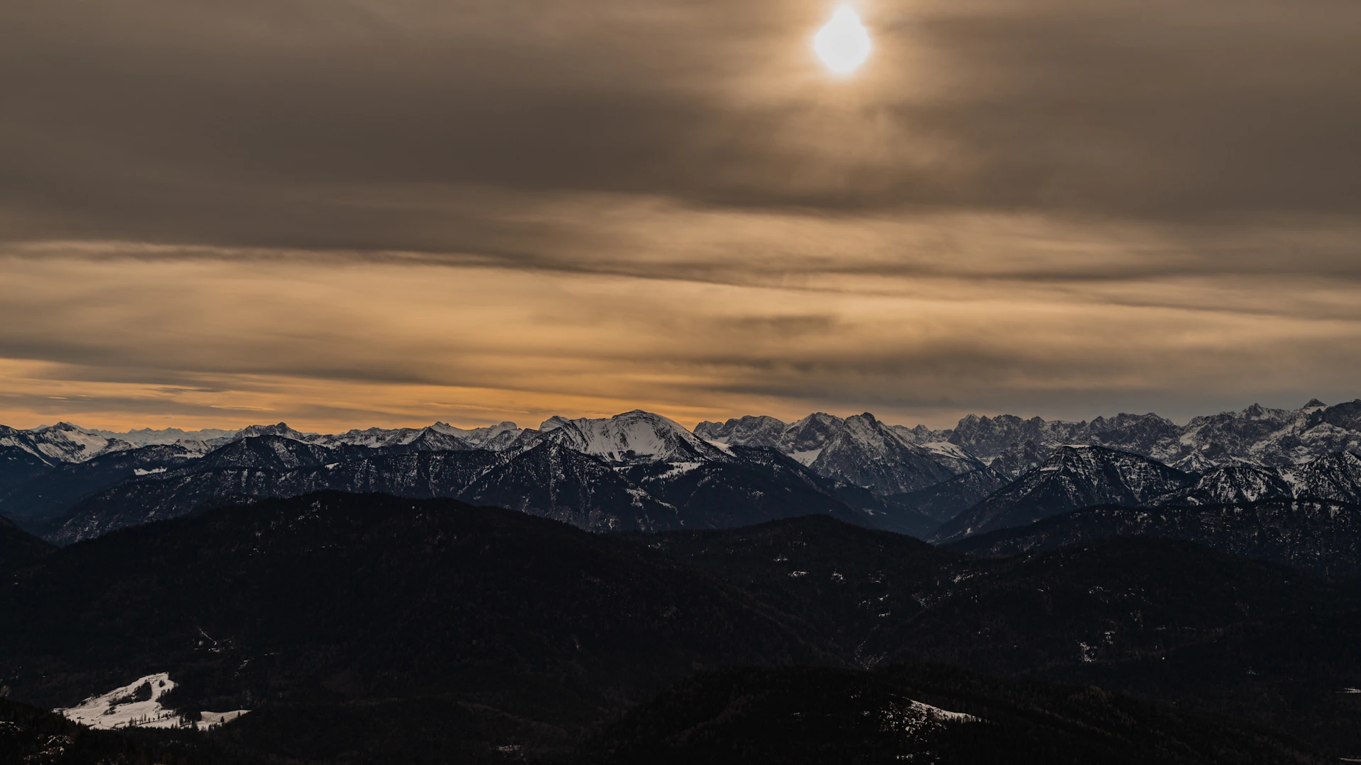 A view of a mountain range with the sun peeking through the clouds