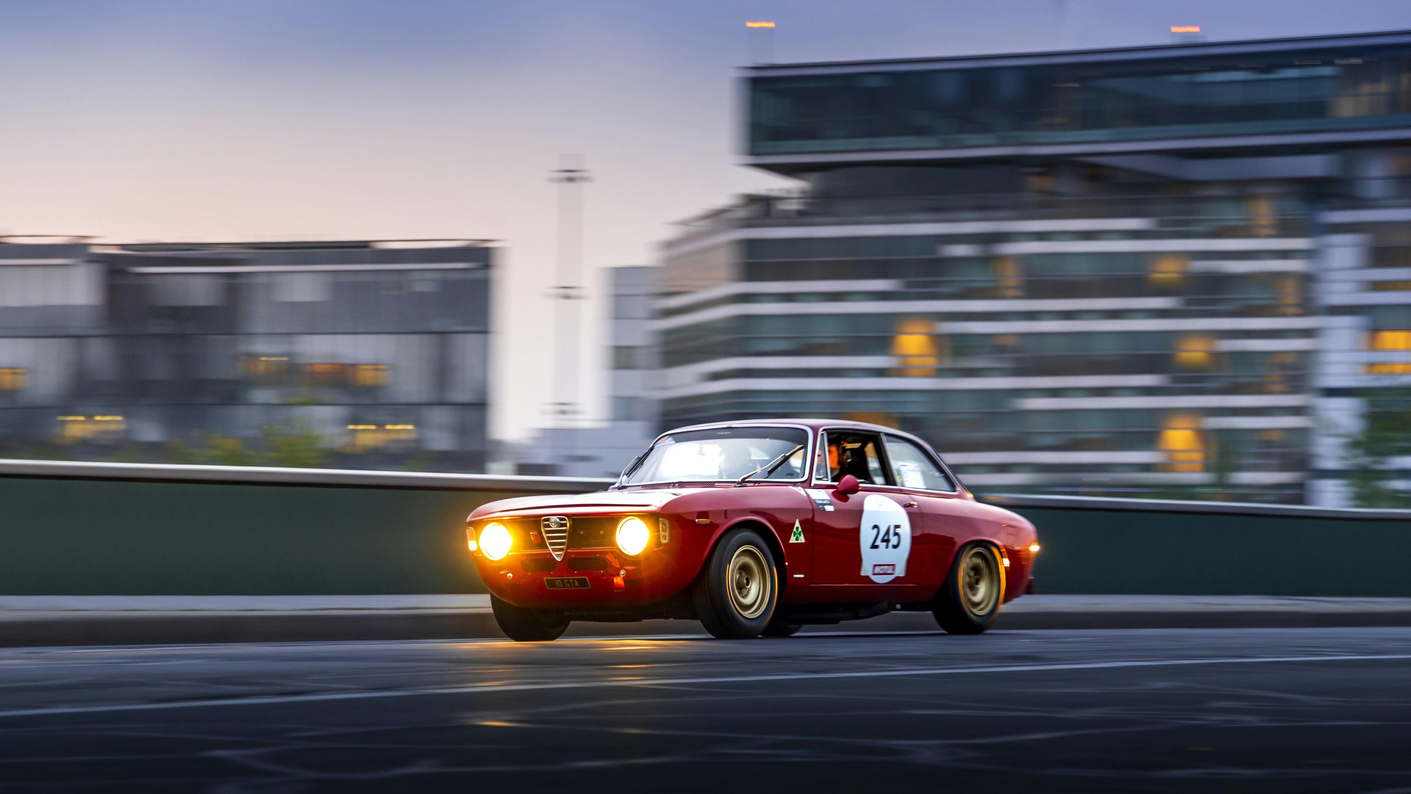 Classic Italian sports car with curved red bodywork on empty mountain road at dusk