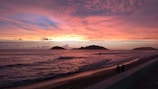 A sunset over the ocean with people walking on the beach