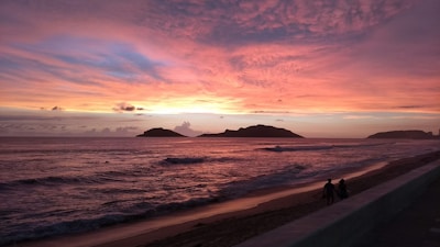 A sunset over the ocean with people walking on the beach