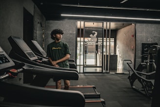 A man standing in a gym next to a row of treadmills