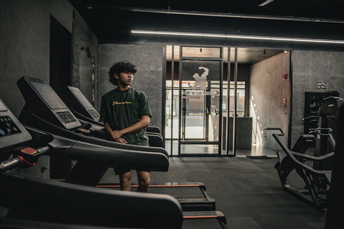 A man standing in a gym next to a row of treadmills