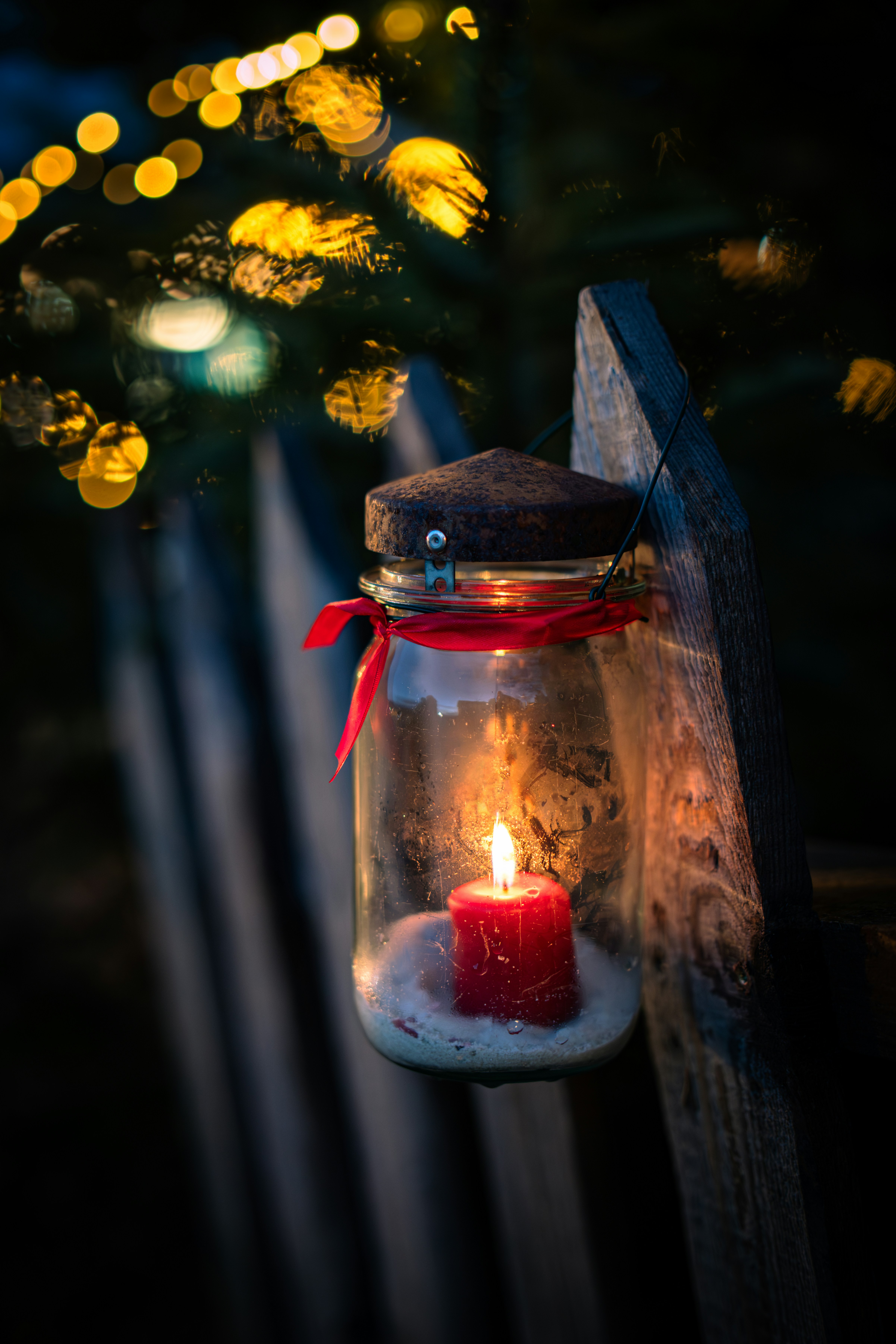 A lit candle in a glass jar on a fence