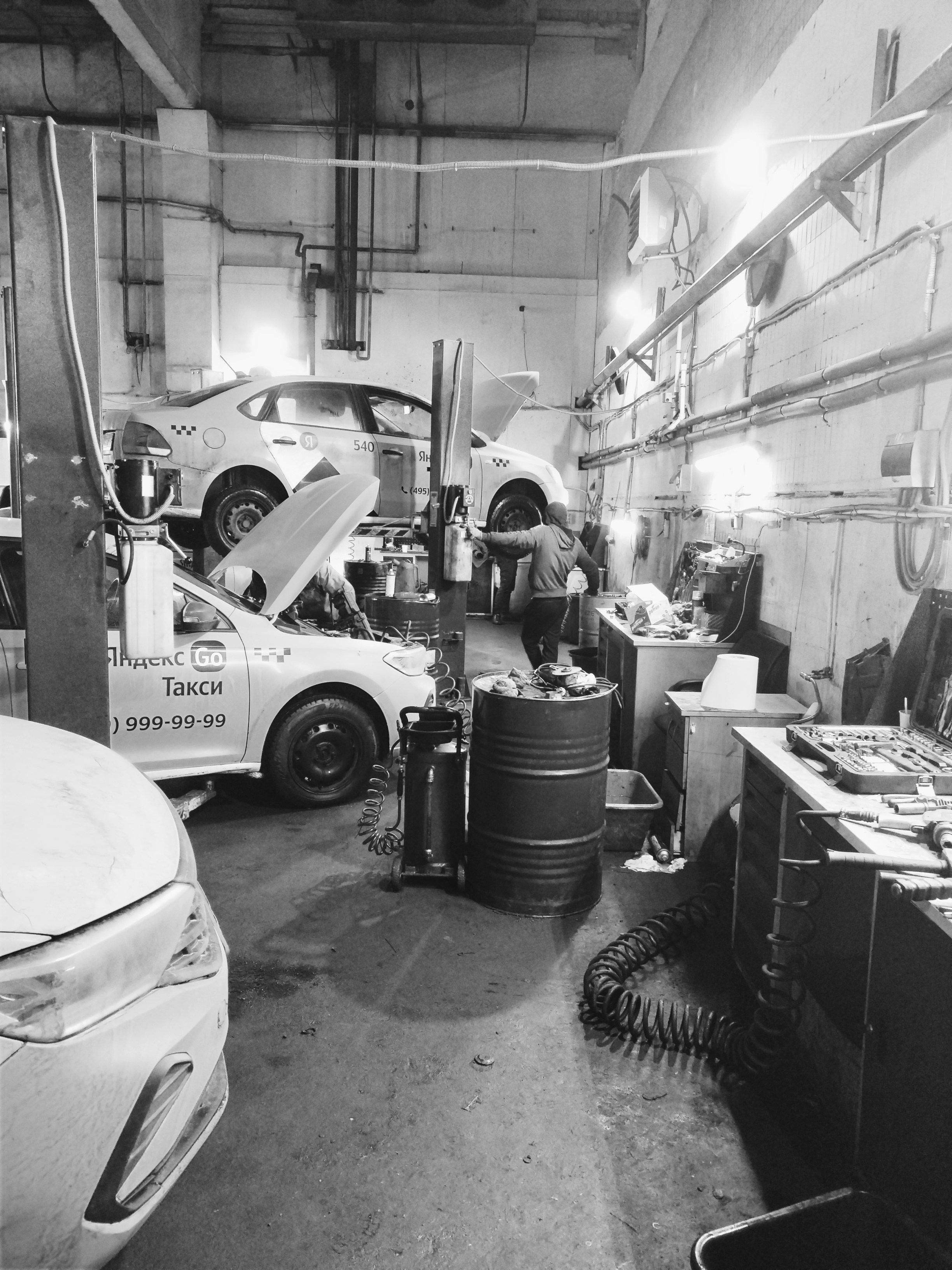 Mecanici auto în service colaborând, iluminat industrial cu umbre profunde și atmosferă de lucru intensă