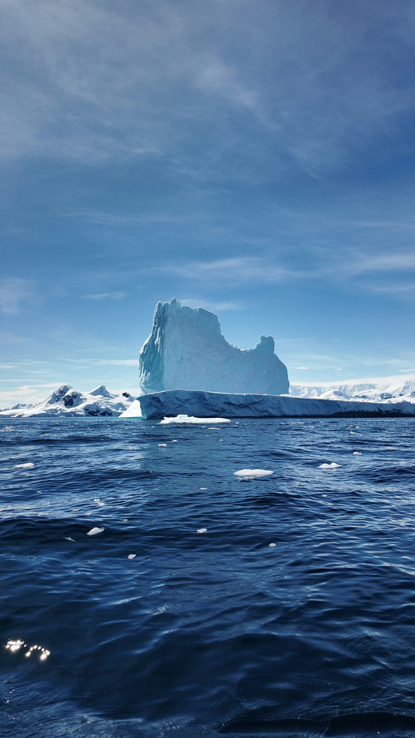 An iceberg floating in the ocean with a blue sky