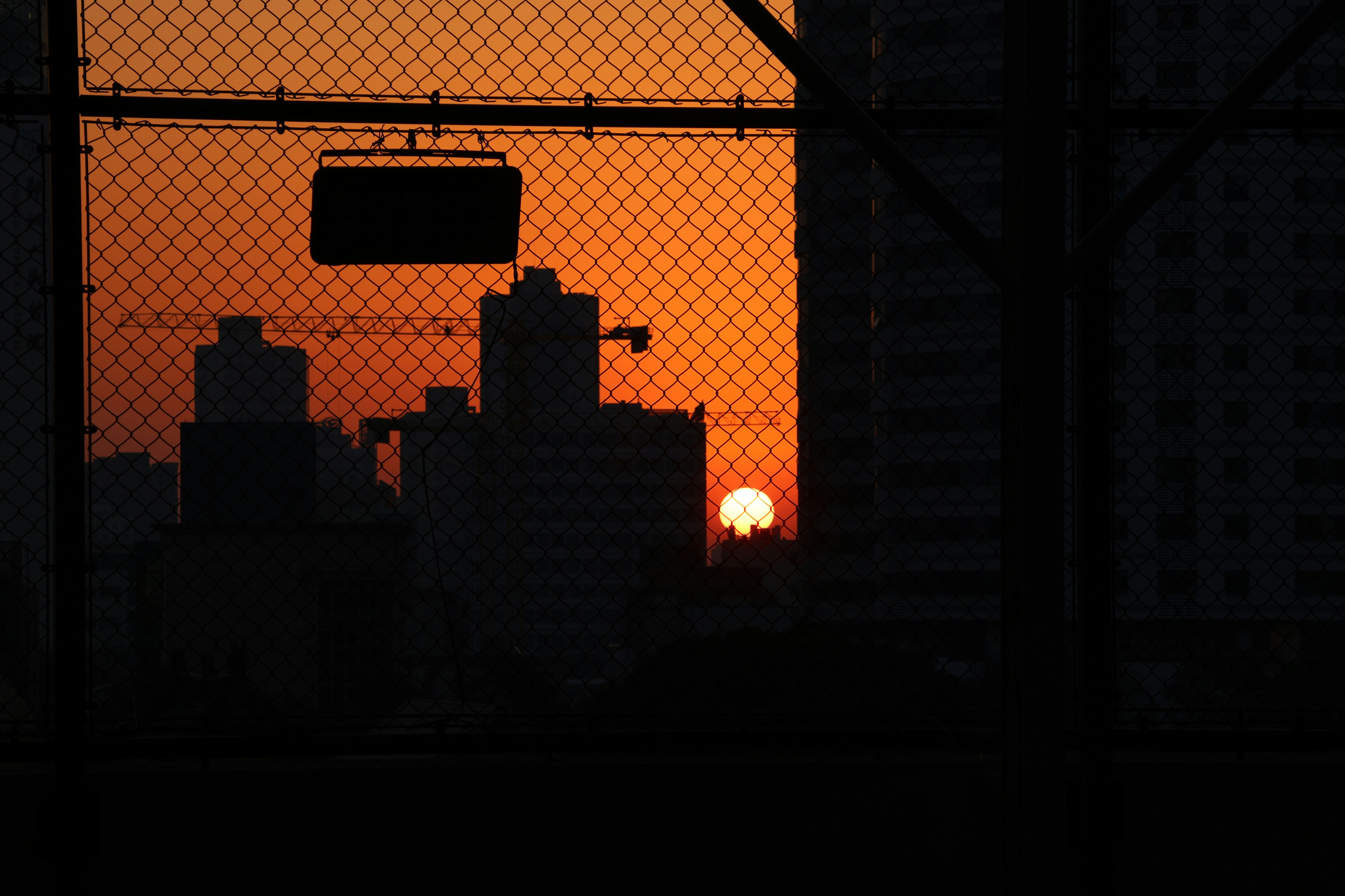 The sun is setting behind a wire fence
