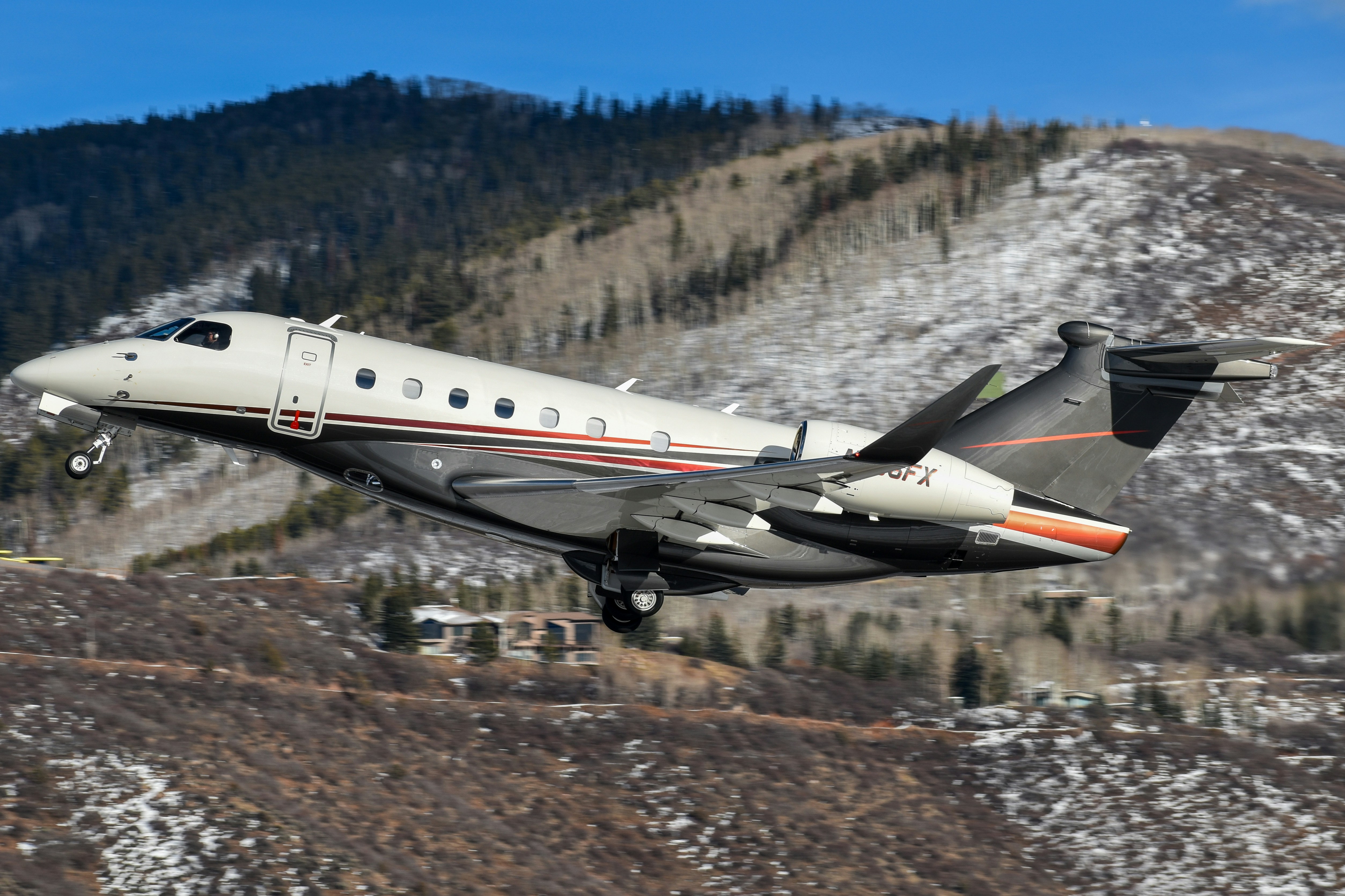 A small plane is flying low to the ground, Flexjet Embraer Praetor 600 departing Aspen/Pitkin County Airport