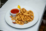 A plate of onion rings with ketchup and a lemon wedge