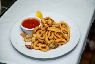 A plate of onion rings with ketchup and a lemon wedge