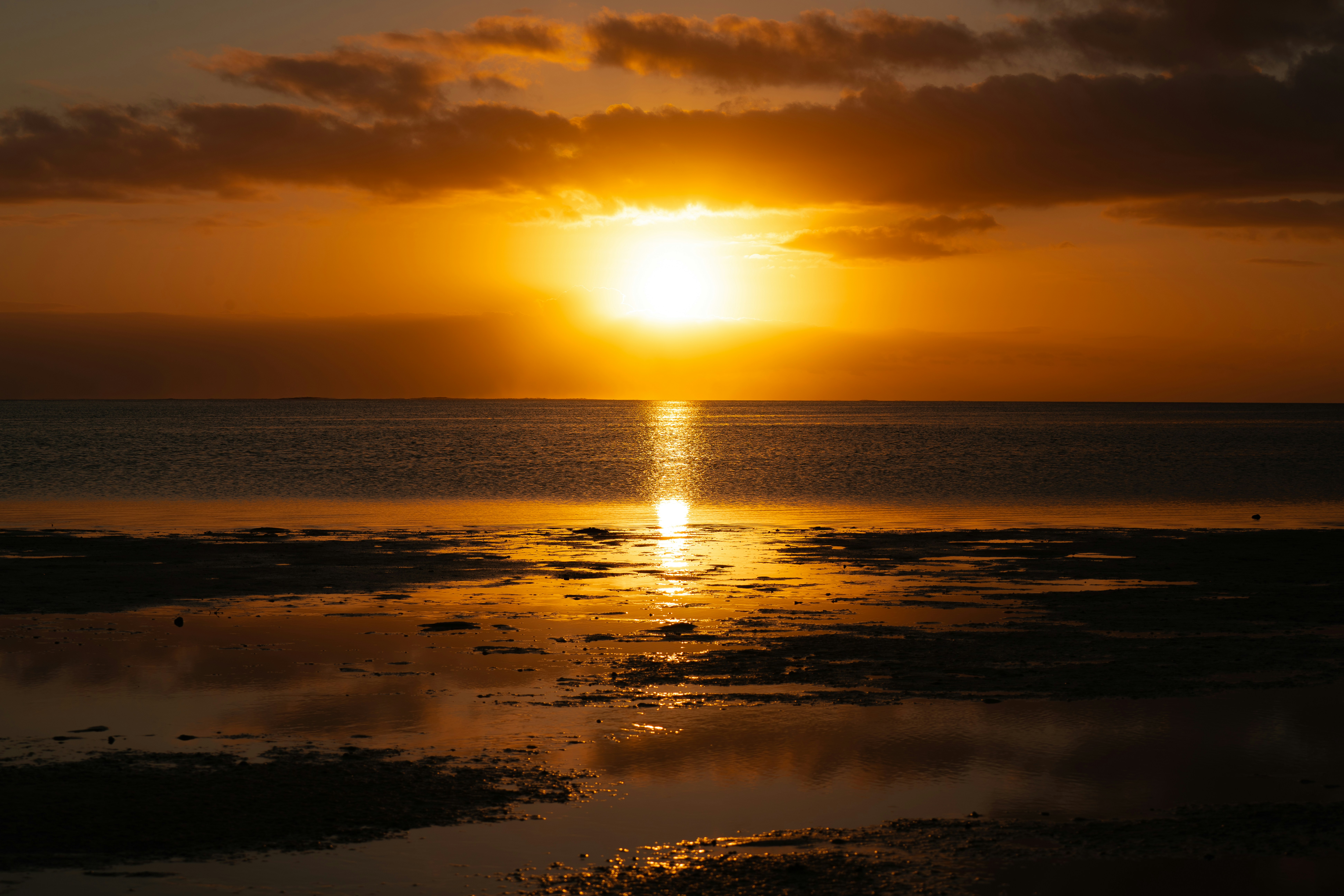 The sun is setting over the water on the beach