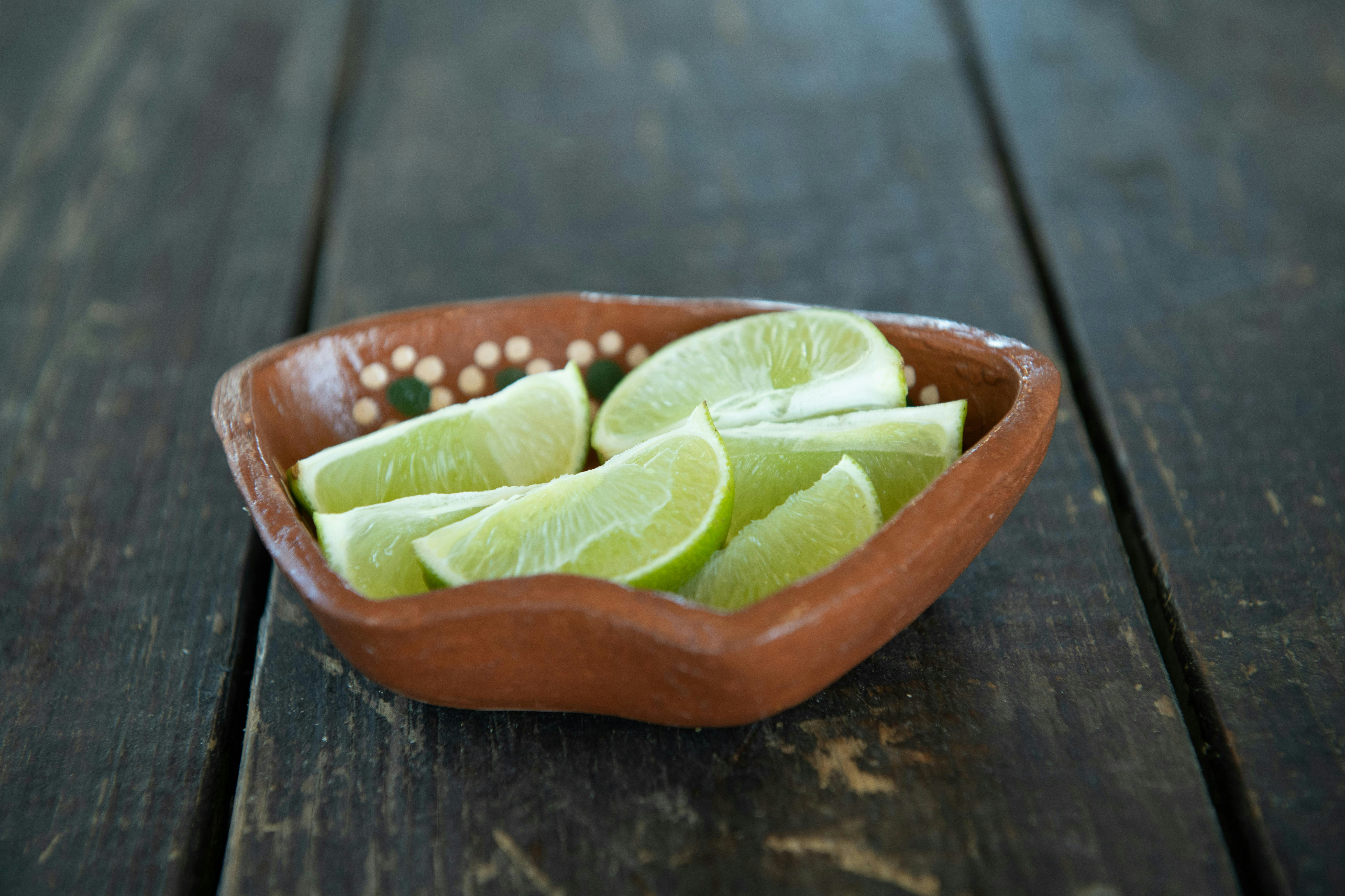 A wooden bowl filled with sliced limes on top of a wooden table