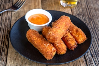 A black plate topped with fried food next to a cup of dipping sauce