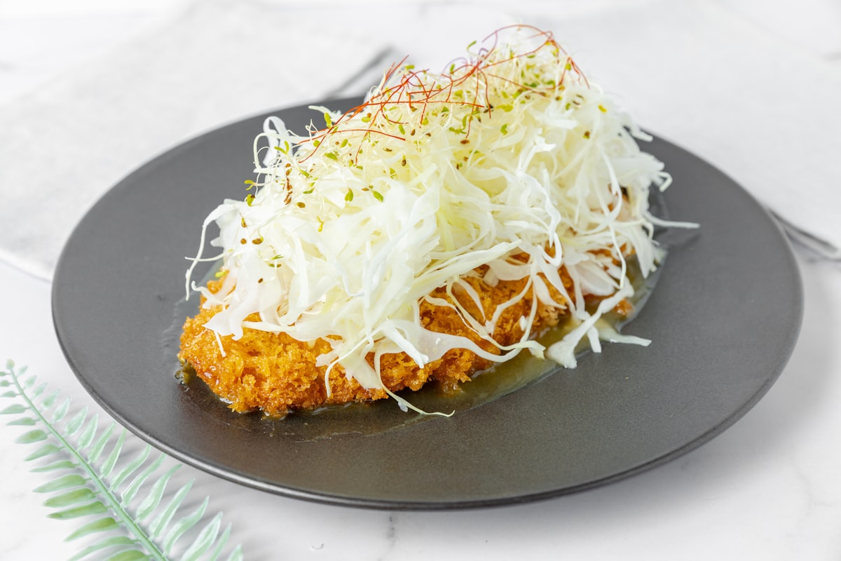 Japanese tonkatsu — golden breaded pork cutlet served on a dark plate with shredded cabbage