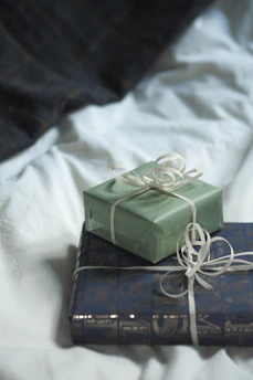 Two wrapped presents sitting on top of each other on a bed