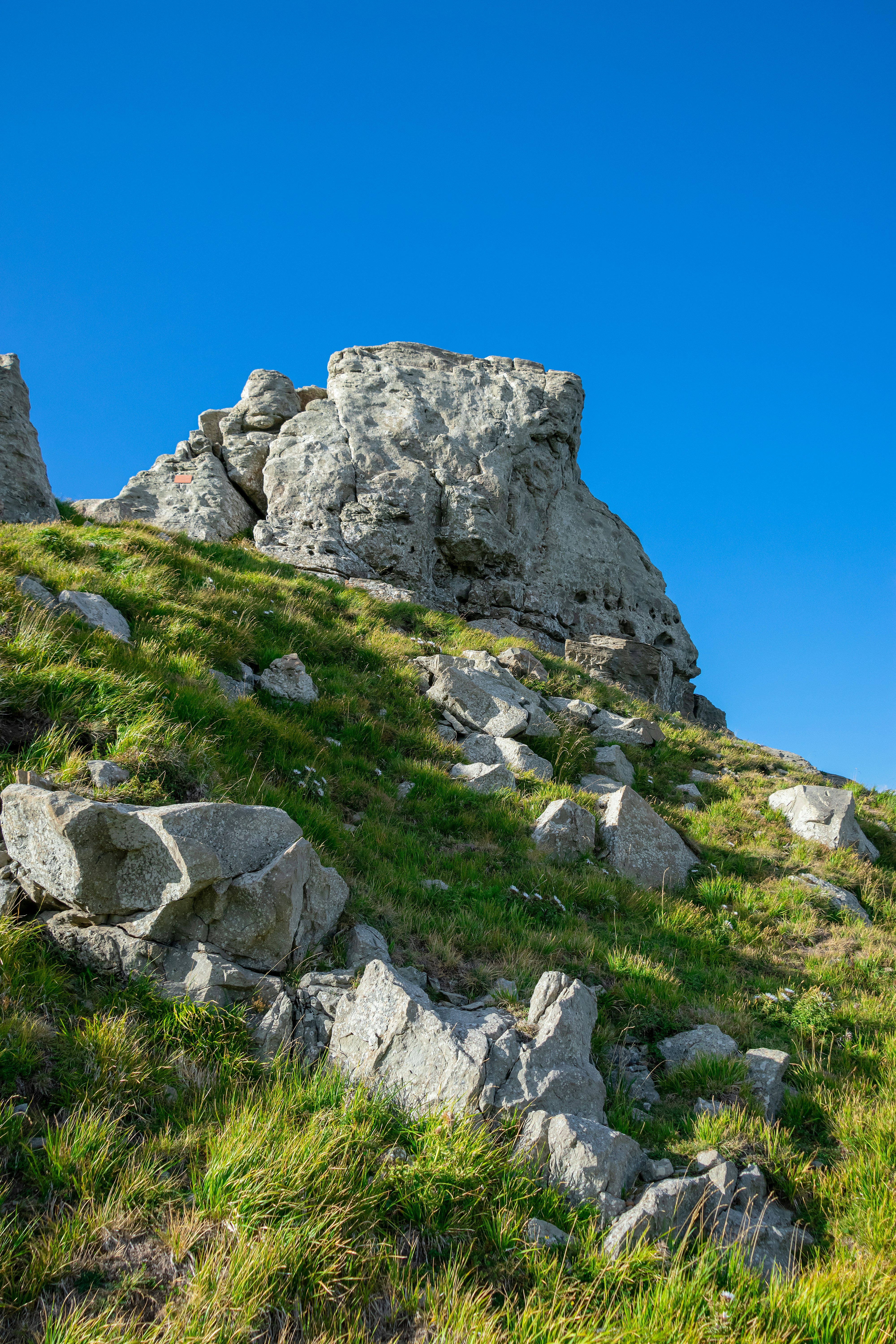 A rocky hill with grass and rocks under a blue sky