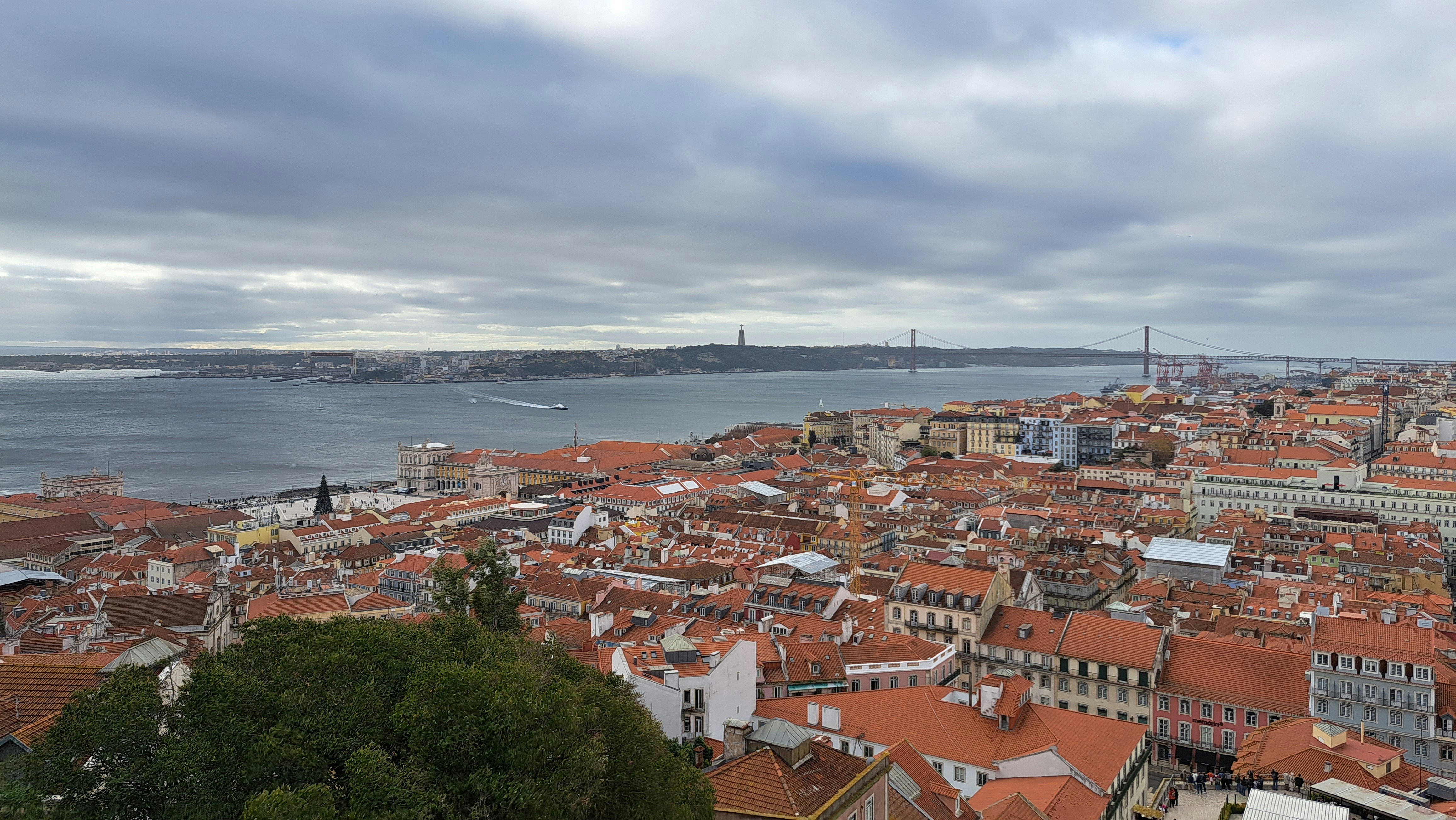 Lisbon cityscape at golden hour, warm amber light, terracotta rooftops, Tagus river in background, deep shadows, atmospheric haze