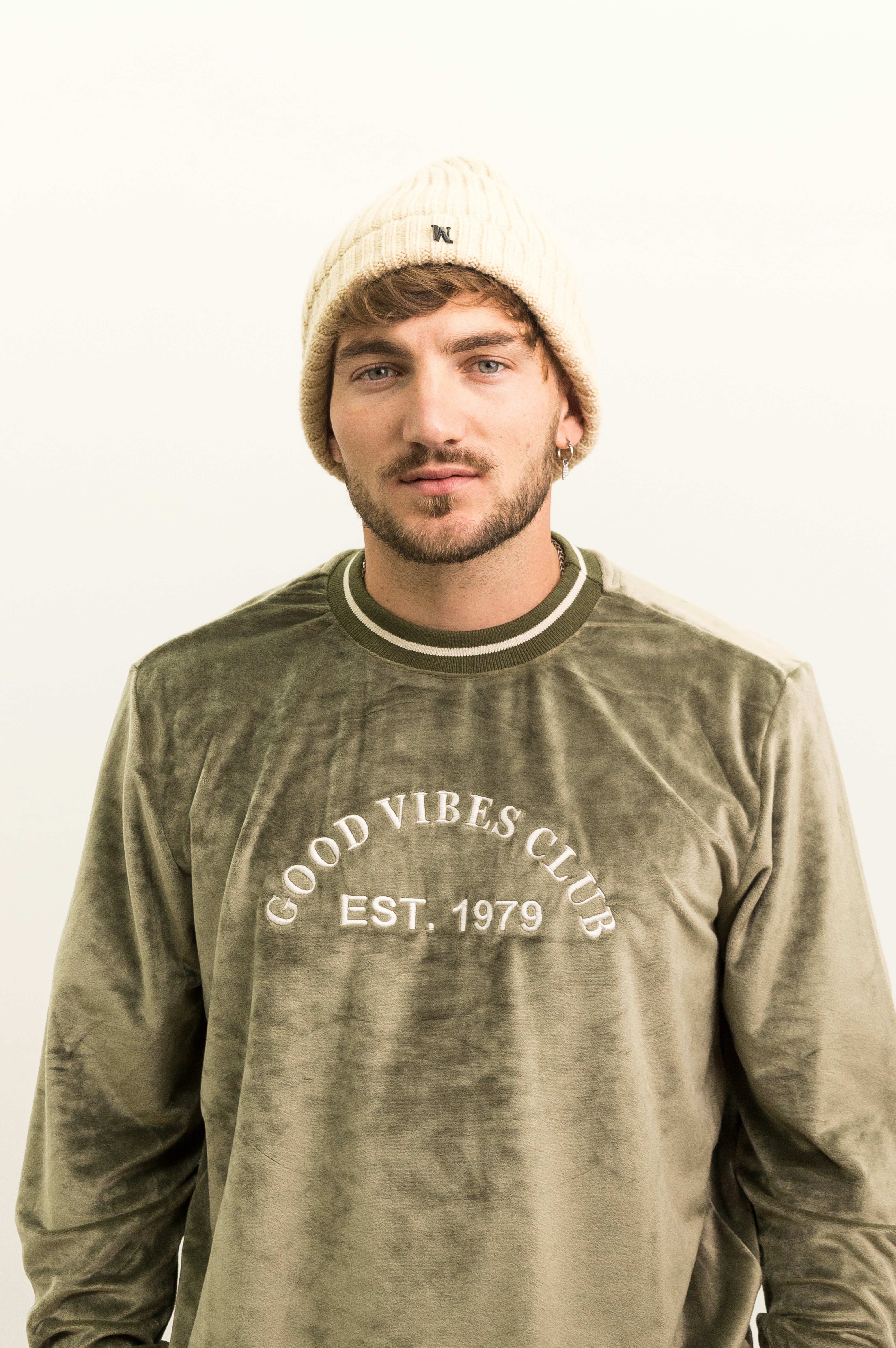 A man wearing a hat standing in front of a white wall
