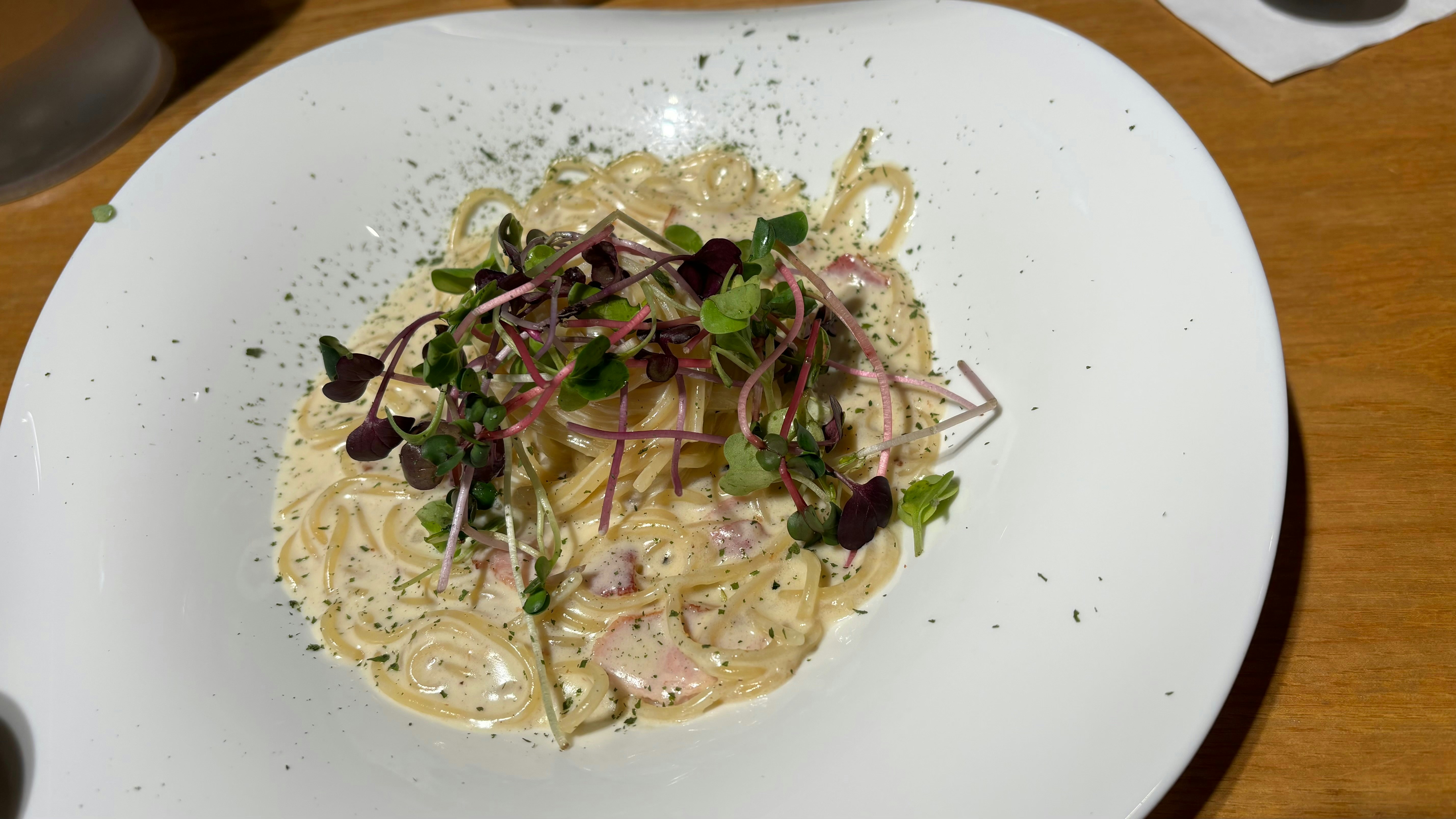 Creamy pasta carbonara with pancetta and parmesan in white bowl on rustic wood table