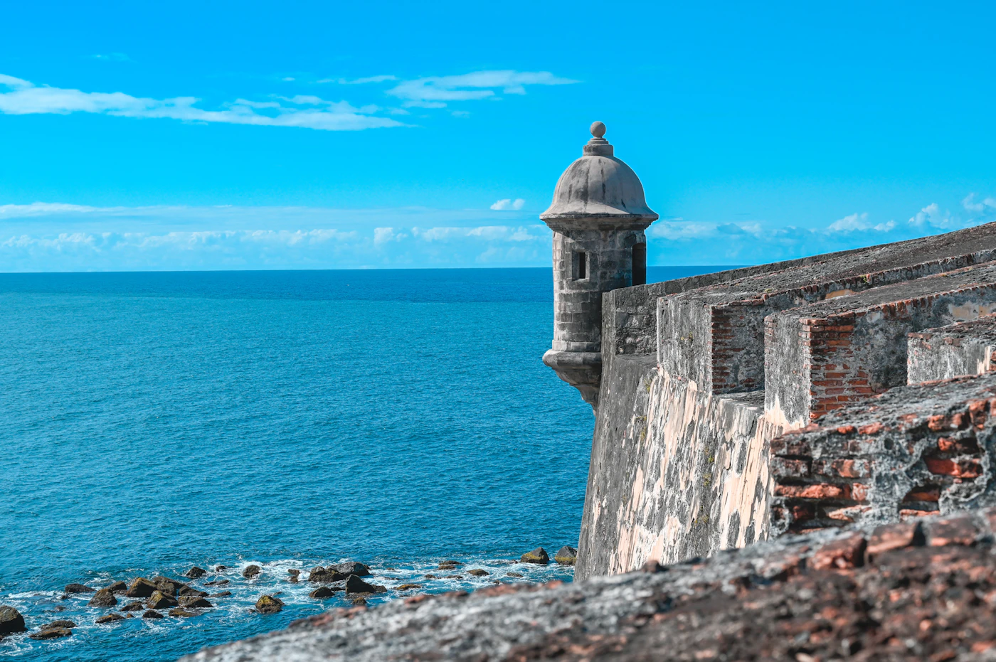An ocean view through the stone walls and arched fortification window of a historic Spanish colonial fort in Puerto Rico with the turquoise Atlantic visible beyond the ancient masonry