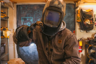 A man in a welding helmet working on a piece of metal for weld cert test 