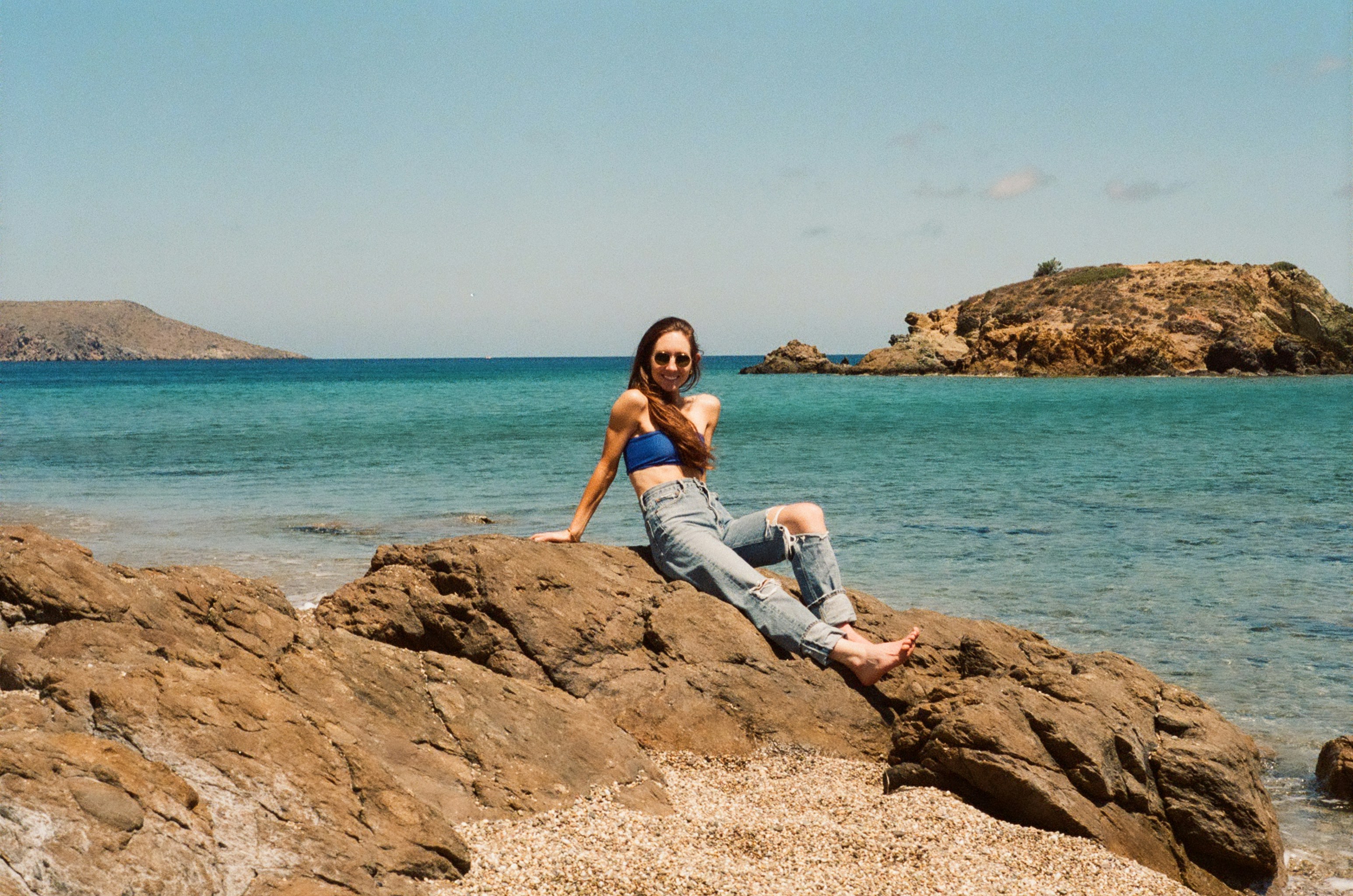 A woman sitting on top of a rock near the ocean