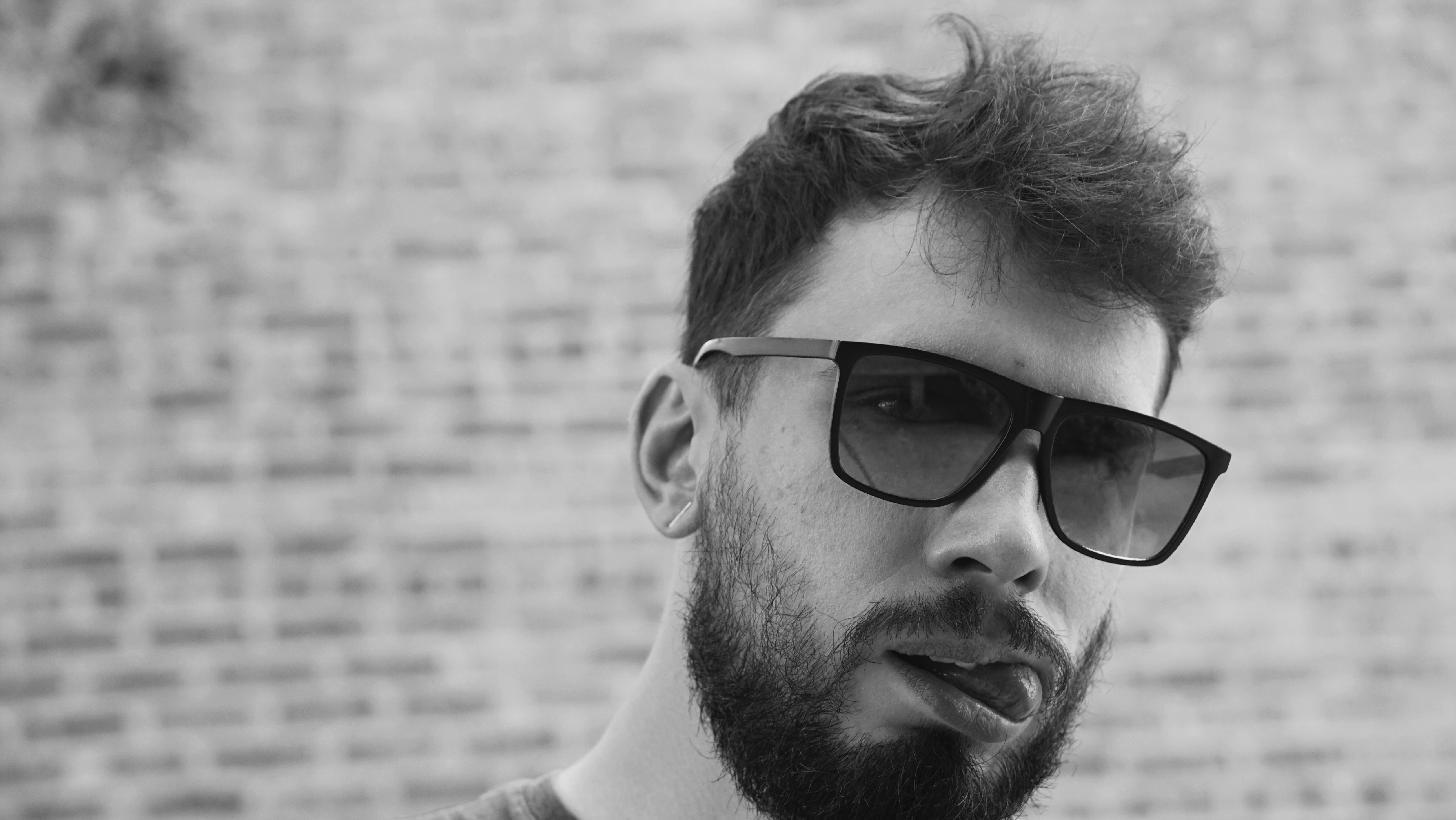A man with a beard and sunglasses standing in front of a brick wall