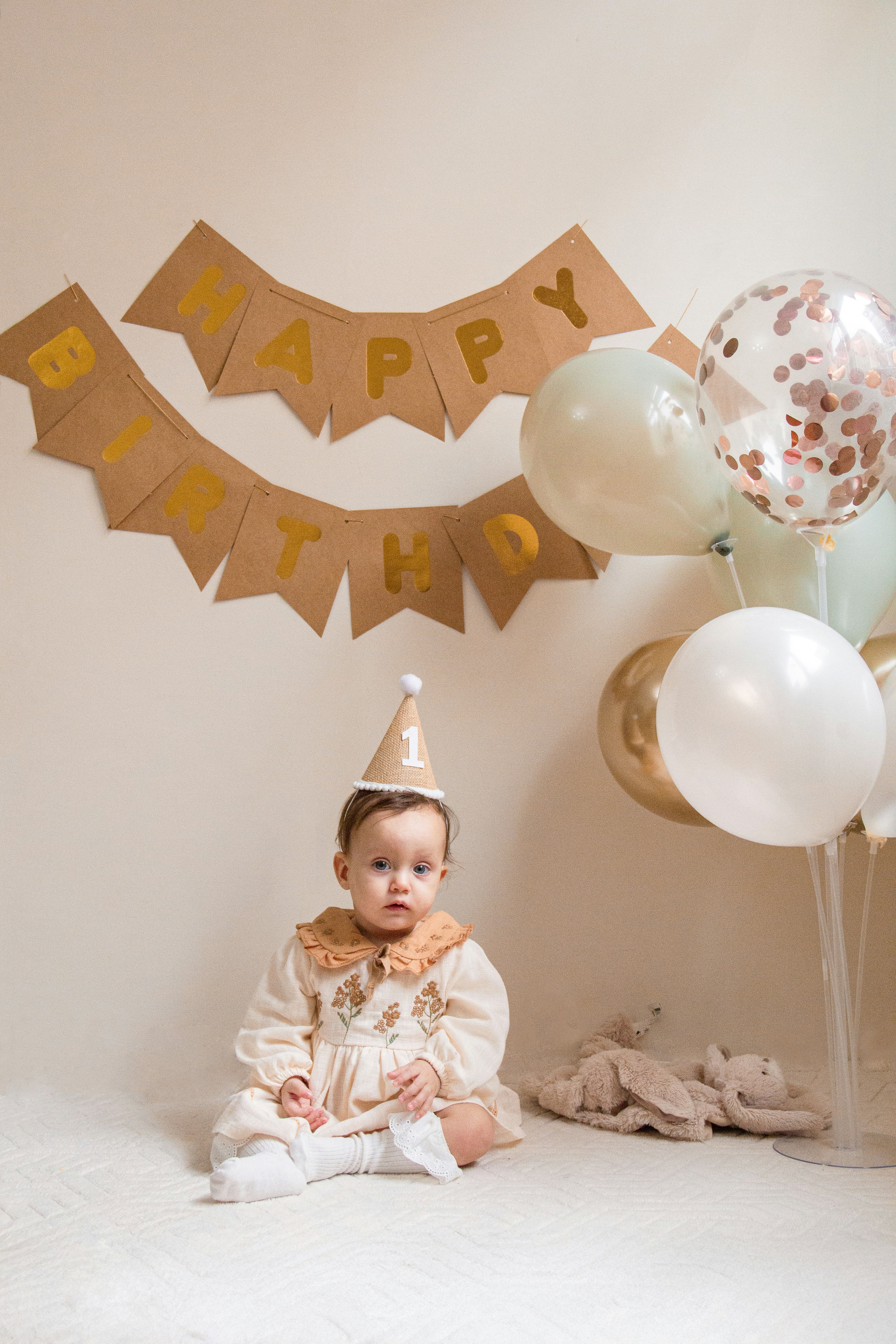 A baby sitting on the floor in front of balloons