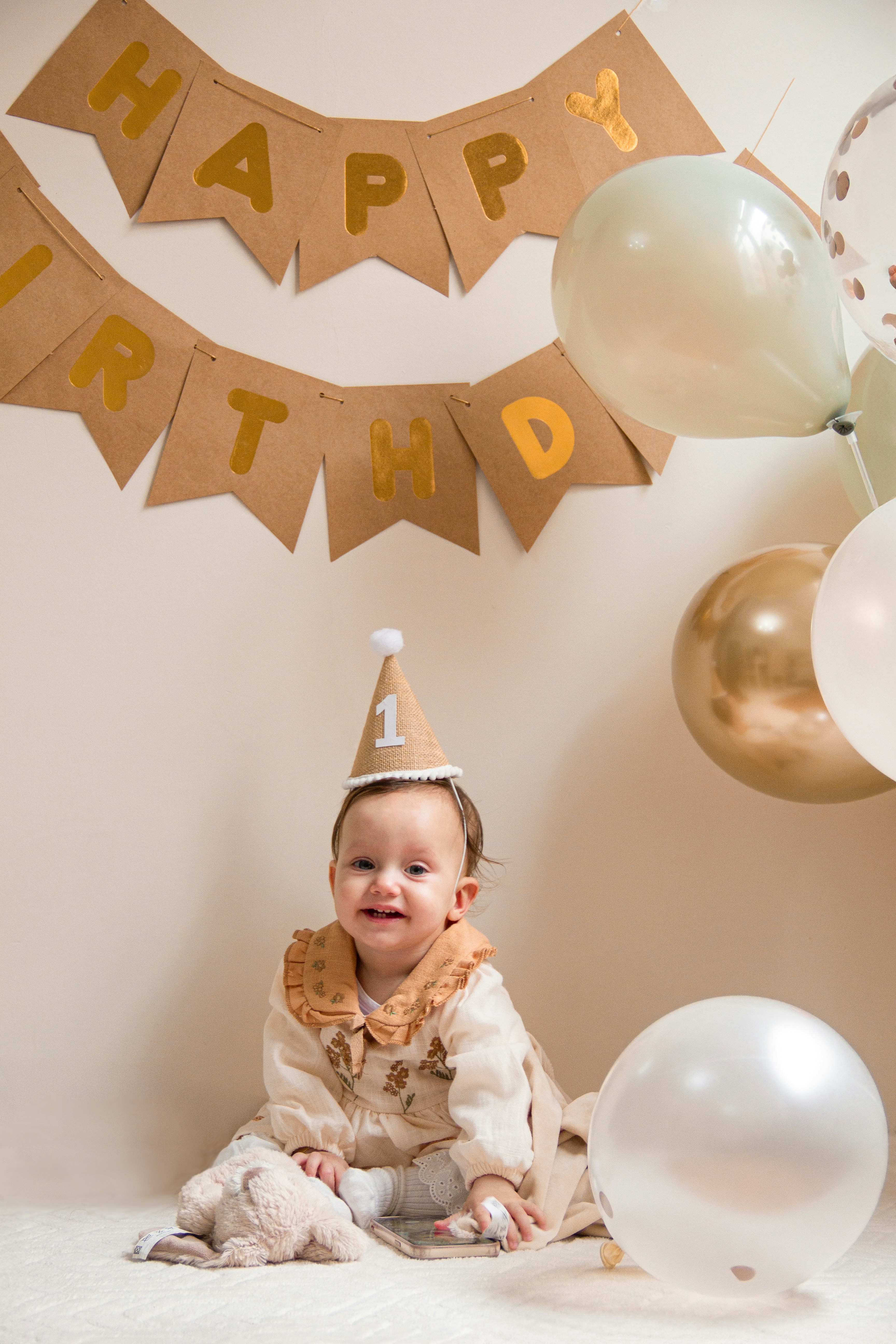 A baby wearing a birthday hat sitting on a bed
