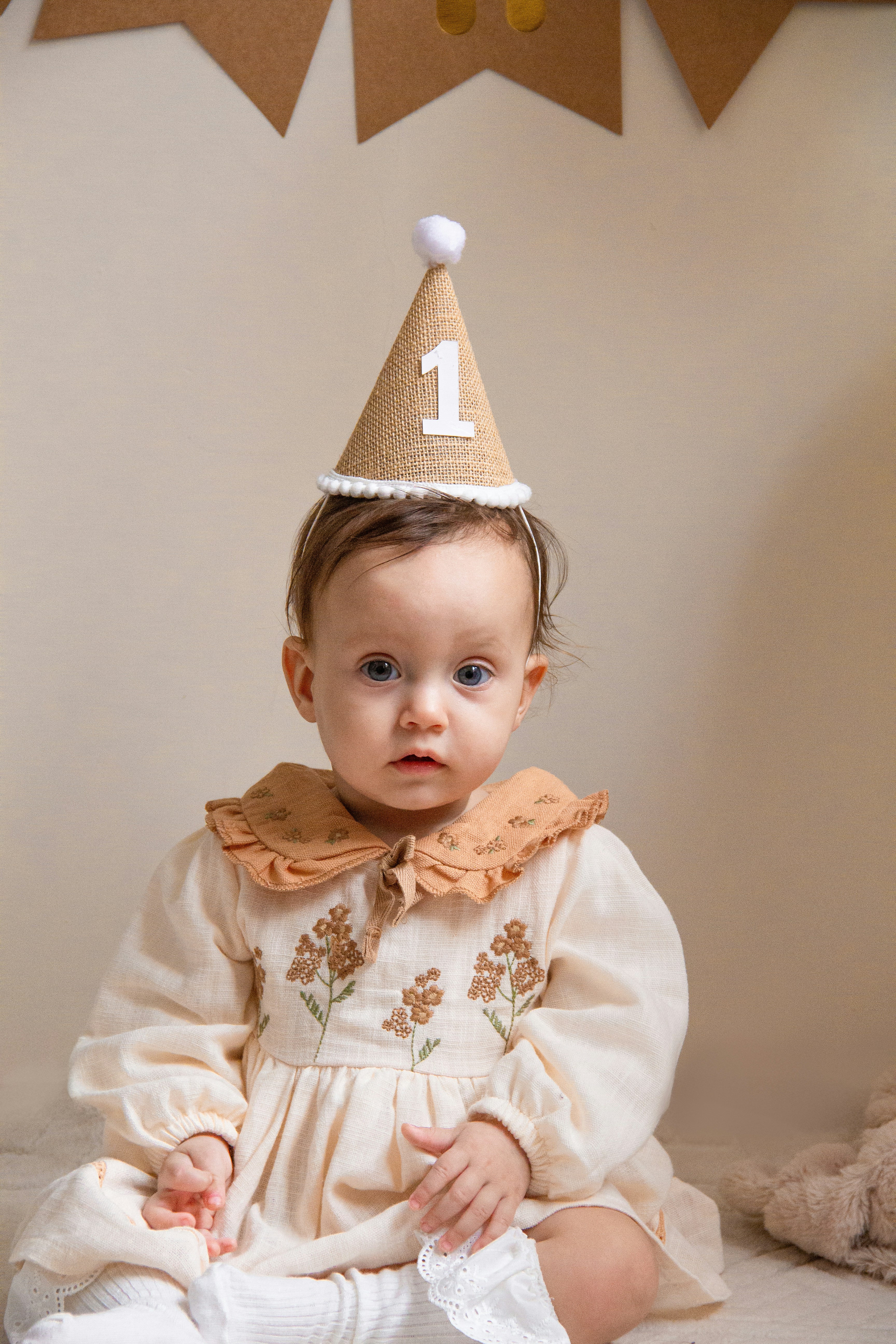 A baby sitting on the floor wearing a birthday hat