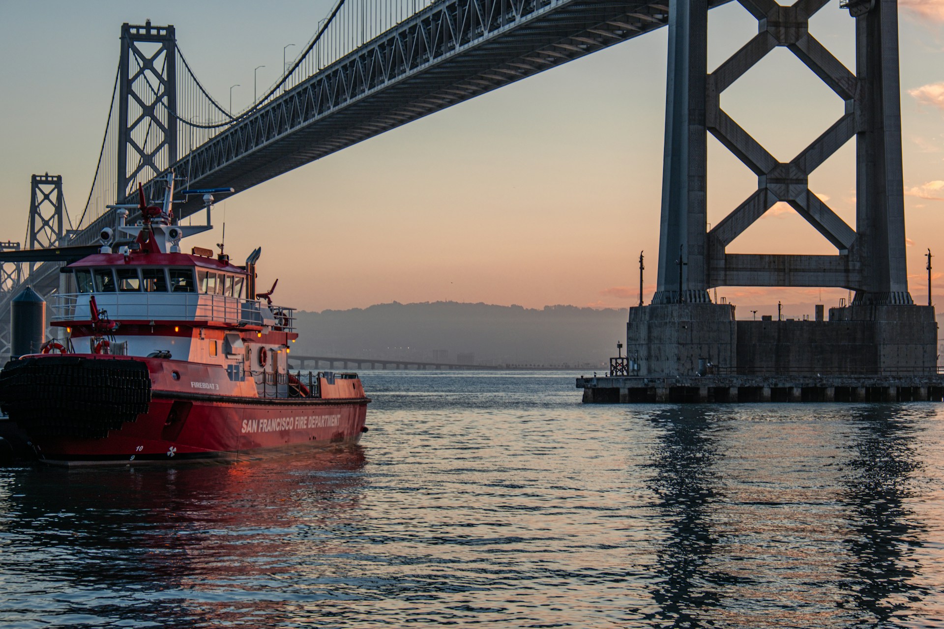 A red boat is in the water under a bridge