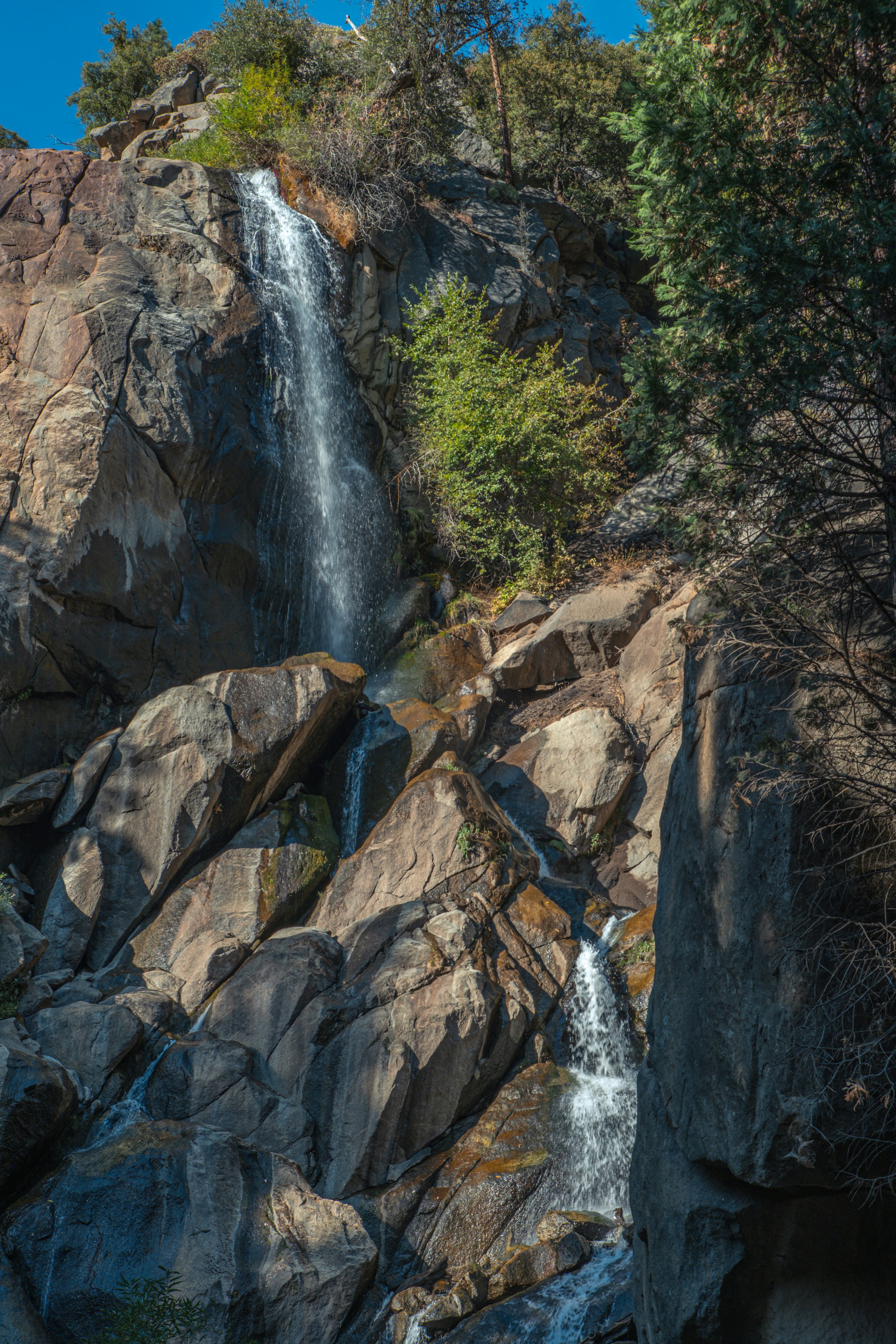 A waterfall is seen from the bottom of a rocky cliff