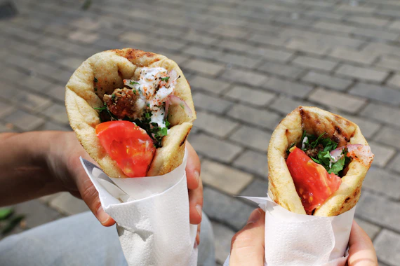 A person holding two gyros in their hands