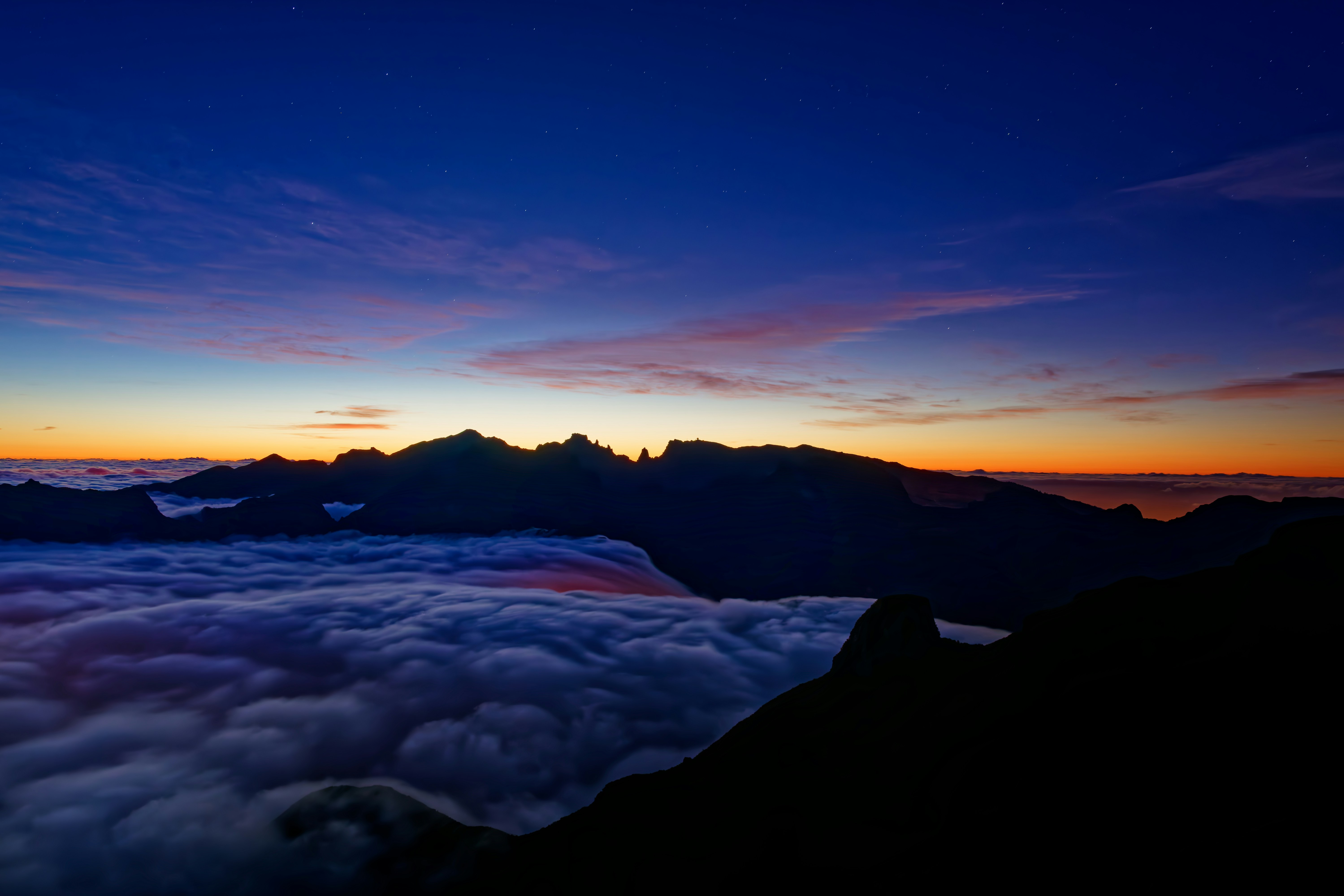 The sun is setting over the clouds and mountains