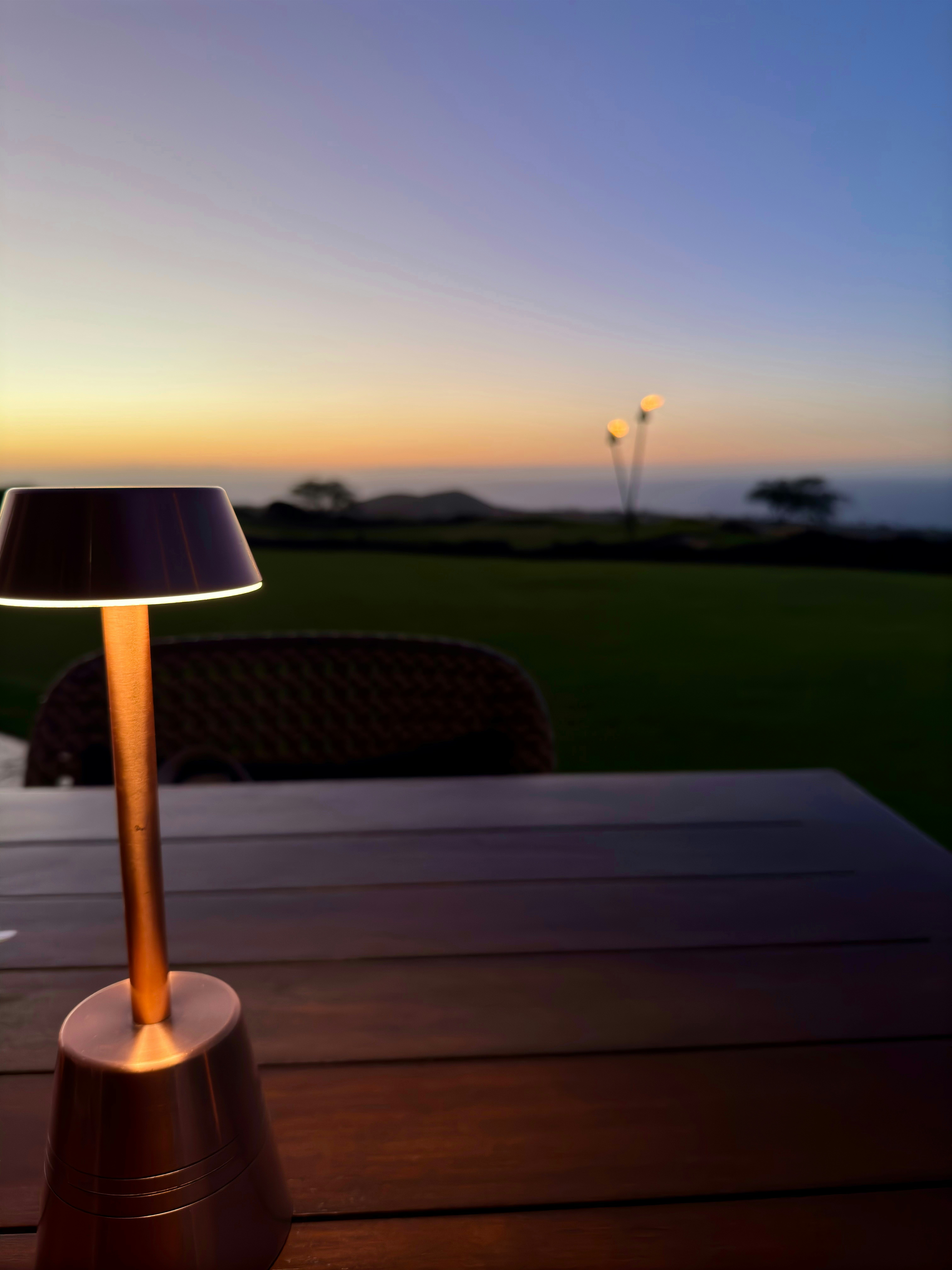 Warm amber reading lamp glowing softly on a wooden campsite table at dusk